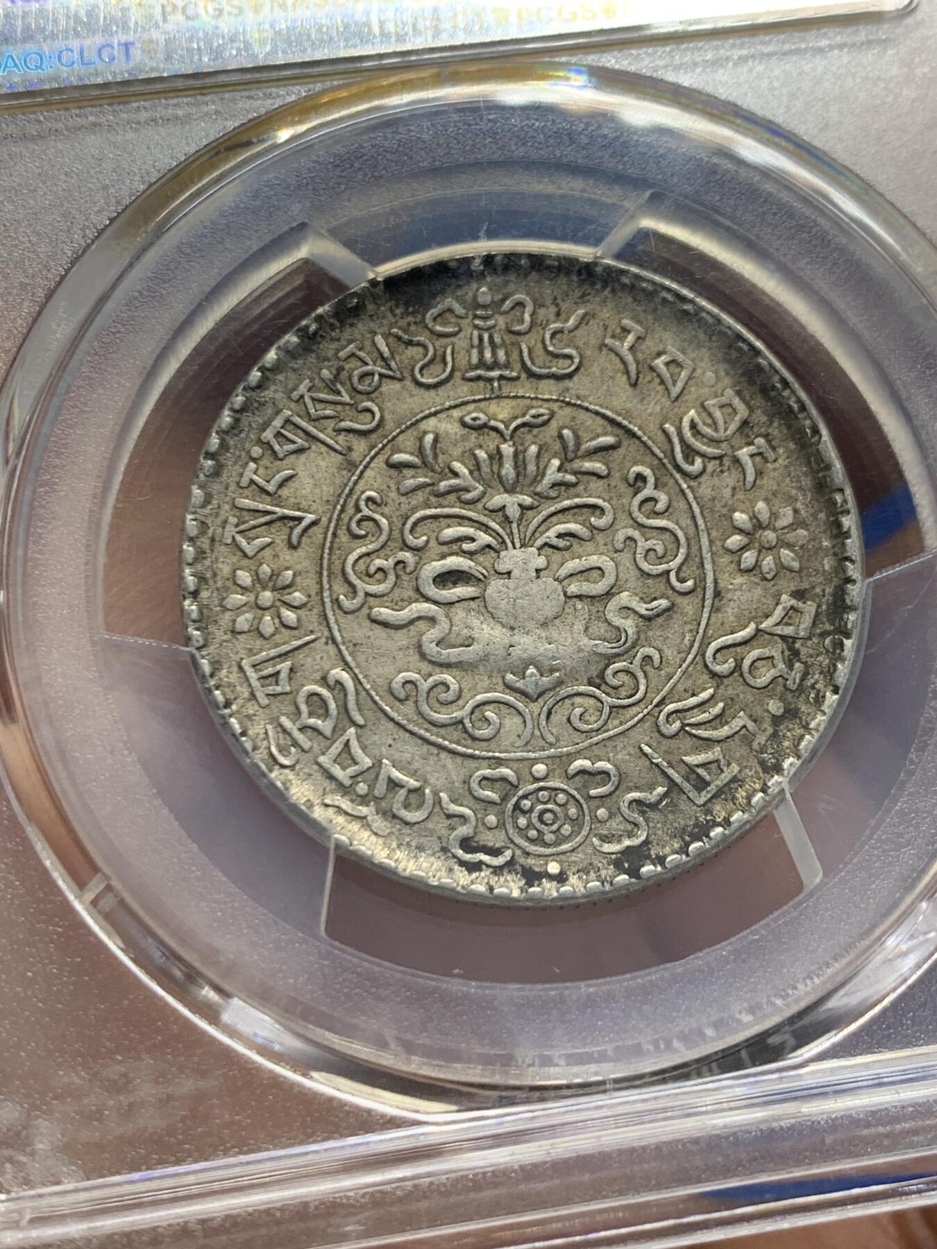 《竞宝斋》第353场 周日，周一，周二 3场连拍 （全场包邮） PCGS AU55 中国1937年西藏桑松果木三两银币，正面中央圆环内为日月、冈仁波齐雪山、祥云、狮子、绣球图案，外圈由宝伞（左上）、宝鱼（右上）、白海螺（右下）、吉祥结（左下）作为间隔环刻藏文“甘丹颇章，战胜四方”字样。背面中央圆环内为花枝和宝瓶图案，周围环绕缠枝纹和飘带；外圈以胜利幢（上）、金法轮（下）和莲花（左右）作为间隔，环刻藏文纪年、面值。具有独特的历史背景、文化内涵和艺术特征。此枚原味