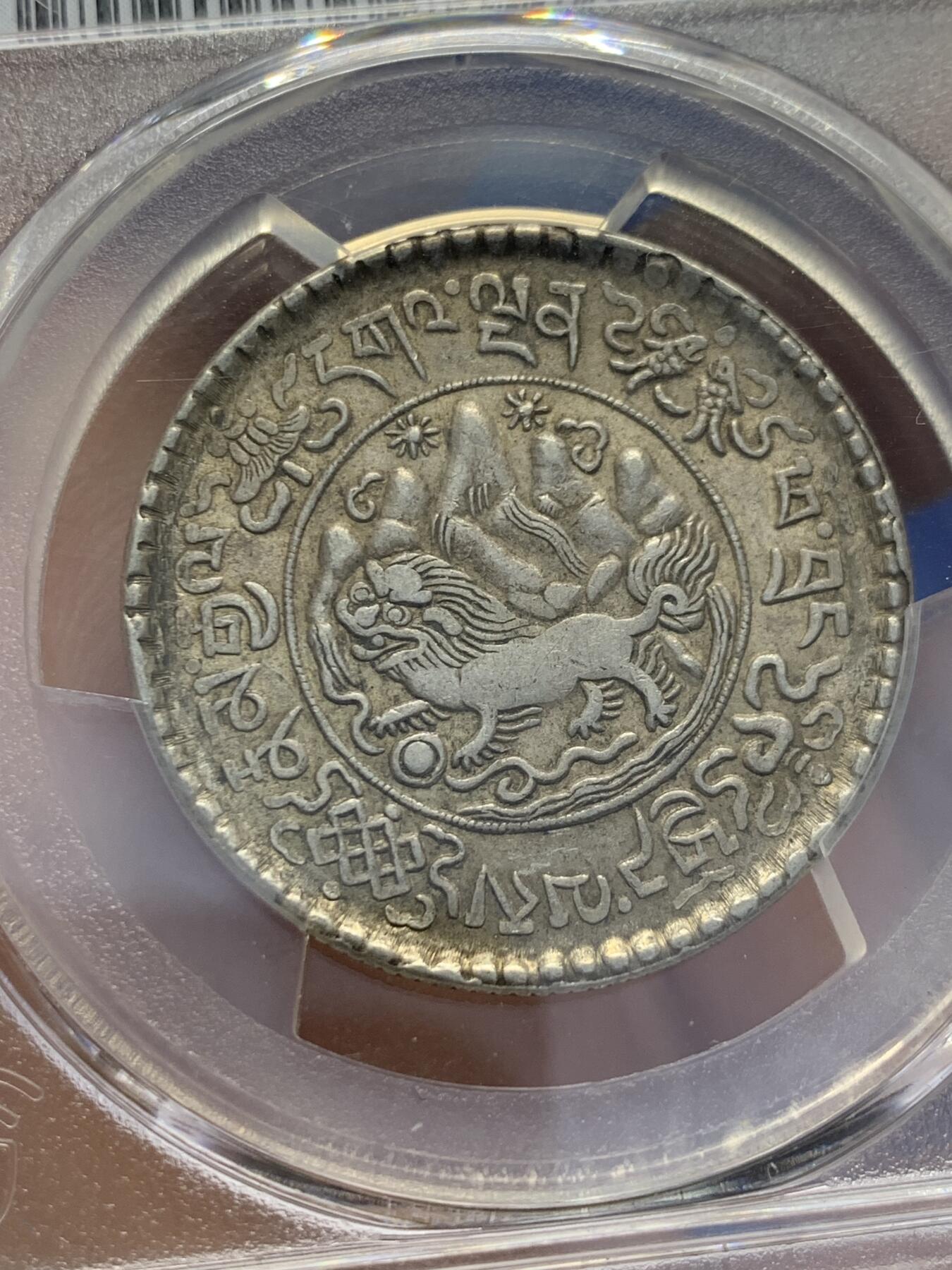 《竞宝斋》第353场 周日，周一，周二 3场连拍 （全场包邮） PCGS AU55 中国1937年西藏桑松果木三两银币，正面中央圆环内为日月、冈仁波齐雪山、祥云、狮子、绣球图案，外圈由宝伞（左上）、宝鱼（右上）、白海螺（右下）、吉祥结（左下）作为间隔环刻藏文“甘丹颇章，战胜四方”字样。背面中央圆环内为花枝和宝瓶图案，周围环绕缠枝纹和飘带；外圈以胜利幢（上）、金法轮（下）和莲花（左右）作为间隔，环刻藏文纪年、面值。具有独特的历史背景、文化内涵和艺术特征。此枚原味