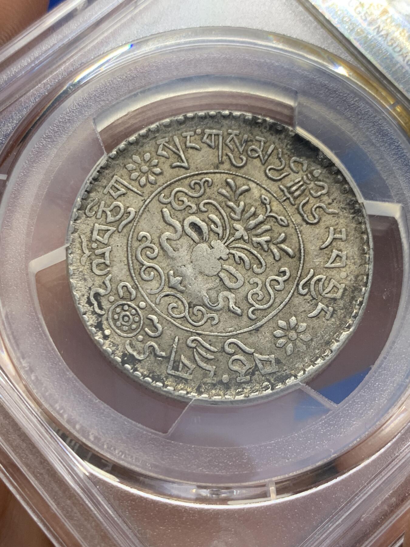 《竞宝斋》第353场 周日，周一，周二 3场连拍 （全场包邮） PCGS AU55 中国1937年西藏桑松果木三两银币，正面中央圆环内为日月、冈仁波齐雪山、祥云、狮子、绣球图案，外圈由宝伞（左上）、宝鱼（右上）、白海螺（右下）、吉祥结（左下）作为间隔环刻藏文“甘丹颇章，战胜四方”字样。背面中央圆环内为花枝和宝瓶图案，周围环绕缠枝纹和飘带；外圈以胜利幢（上）、金法轮（下）和莲花（左右）作为间隔，环刻藏文纪年、面值。具有独特的历史背景、文化内涵和艺术特征。此枚原味