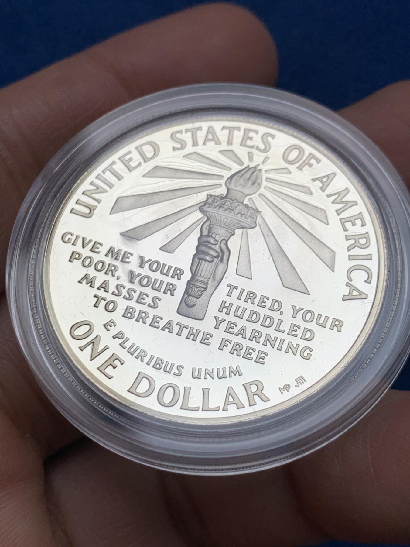 《竞宝斋》第353场 周日，周一，周二 3场连拍 （全场包邮） 美国1986年纪念自由女神像建成100周年精制银币套装。银币正面为庄严肃穆自由女神像，银币反面为自由女神像的火炬以及诗歌《新巨人》中的文字。 半美元铜镍币正面为纽约的天际线，自由女神像举起手臂，迎接一艘驶向纽约的班轮，太阳从东方升起，寓意着新世界新生活的开始。背面图案源自埃利斯岛上等待前往纽约的移民照片，反映了自由女神像作为移民希望象征的意义。