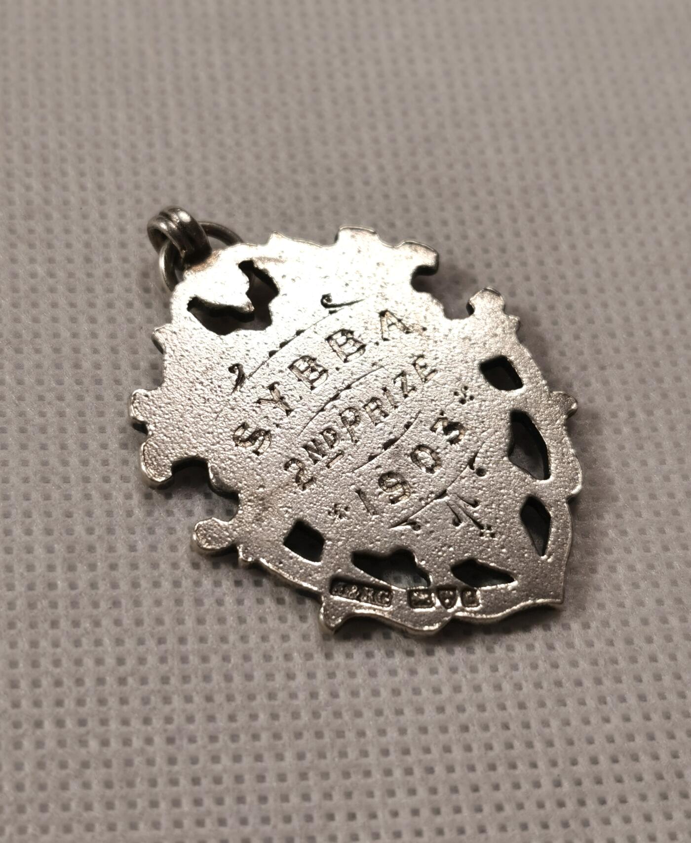  甄臻铺-世界币章拍卖（第19期），送拍享返佣金等优惠多多 1903年SYBBA第二名奖品，来自英国。经典盾牌设计，工艺精美，适合收藏或佩戴。成色良好，有轻微使用痕迹，由银器大师J&RG制作。尺寸42x31.6毫米，重11.7克。