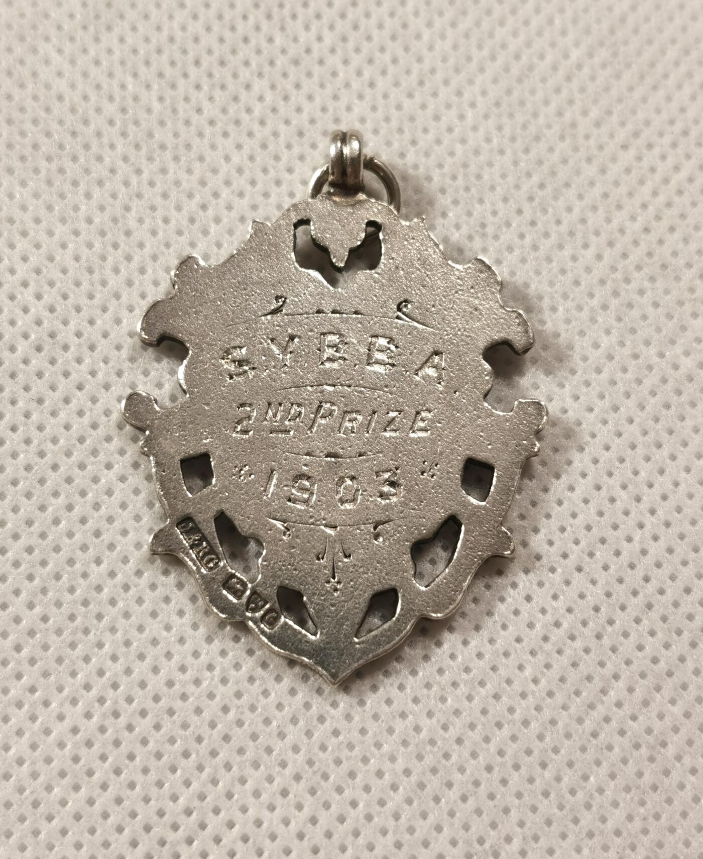  甄臻铺-世界币章拍卖（第19期），送拍享返佣金等优惠多多 1903年SYBBA第二名奖品，来自英国。经典盾牌设计，工艺精美，适合收藏或佩戴。成色良好，有轻微使用痕迹，由银器大师J&RG制作。尺寸42x31.6毫米，重11.7克。