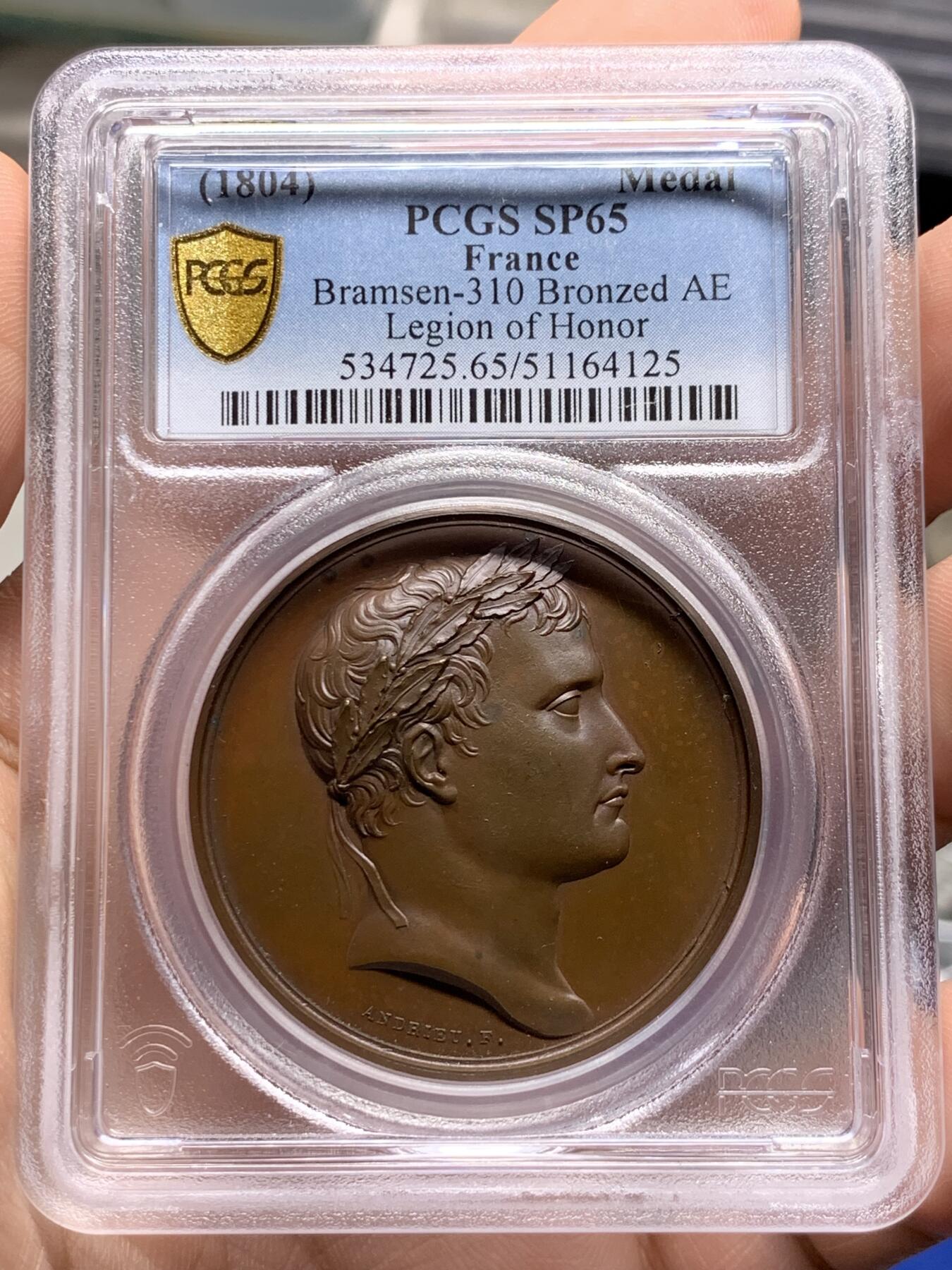 《竞宝斋》第387场 周日，周一 2场连拍 （全场包邮） PCGS SP65 冠军分 法国1804年拿破仑荣誉军团原铸铜章 巴黎造币厂巧克力包浆 荣誉军团勋章交织在月桂树和橡树花环间 ，创造性地将这样一枚传奇的勋章呈现于铜章之上，创意十足远超时代，上部佩环，中间是拿破仑鹰徽和该勋章的铭文 Honneur et Patrie（“荣誉和祖国”），是法国最高的功绩勋章，由拿破仑本人于1802年创立，高浮雕品相顶级 ，属于拿章中的稀少名誉品种。加厚盒。