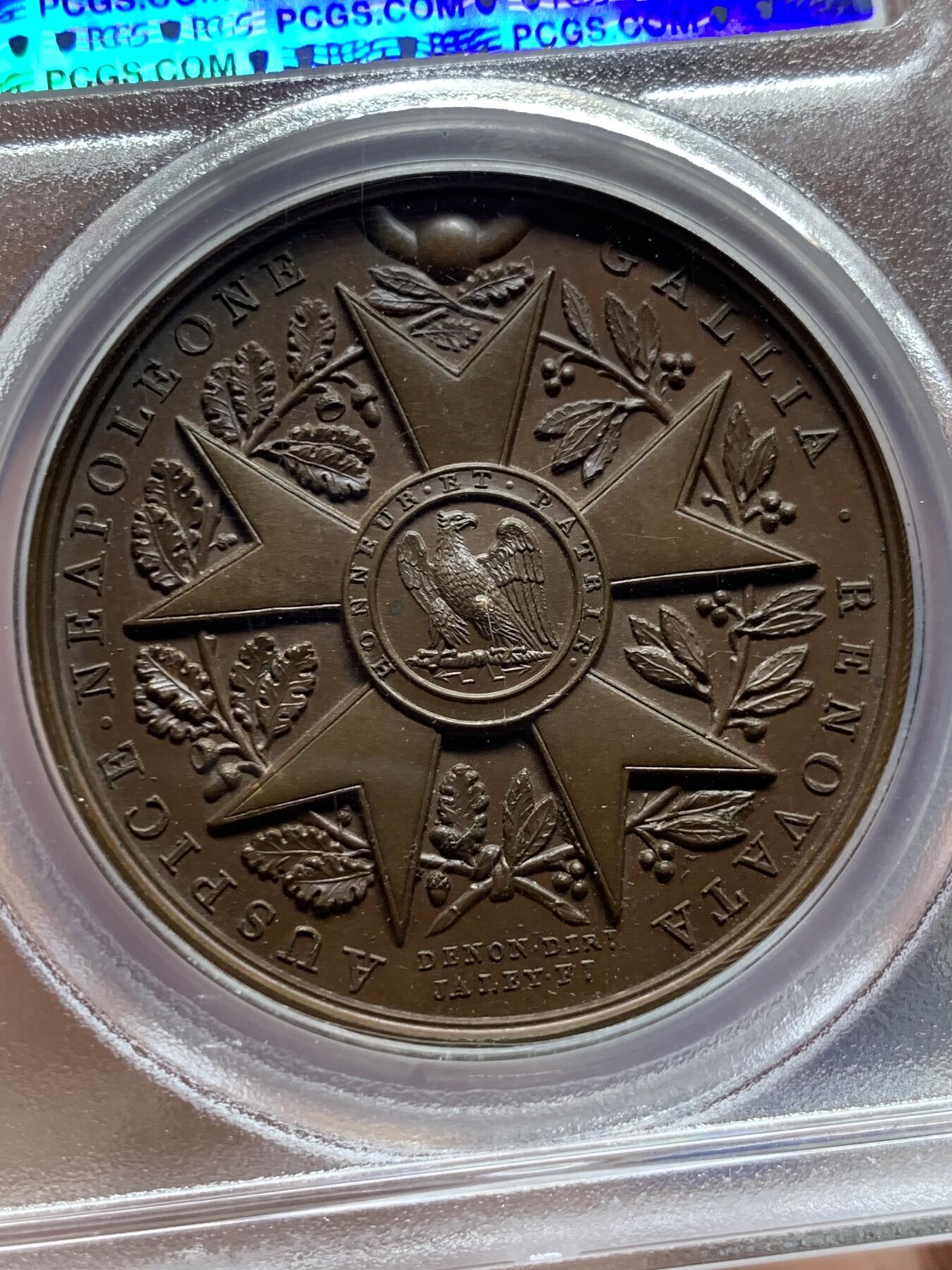 《竞宝斋》第387场 周日，周一 2场连拍 （全场包邮） PCGS SP65 冠军分 法国1804年拿破仑荣誉军团原铸铜章 巴黎造币厂巧克力包浆 荣誉军团勋章交织在月桂树和橡树花环间 ，创造性地将这样一枚传奇的勋章呈现于铜章之上，创意十足远超时代，上部佩环，中间是拿破仑鹰徽和该勋章的铭文 Honneur et Patrie（“荣誉和祖国”），是法国最高的功绩勋章，由拿破仑本人于1802年创立，高浮雕品相顶级 ，属于拿章中的稀少名誉品种。加厚盒。