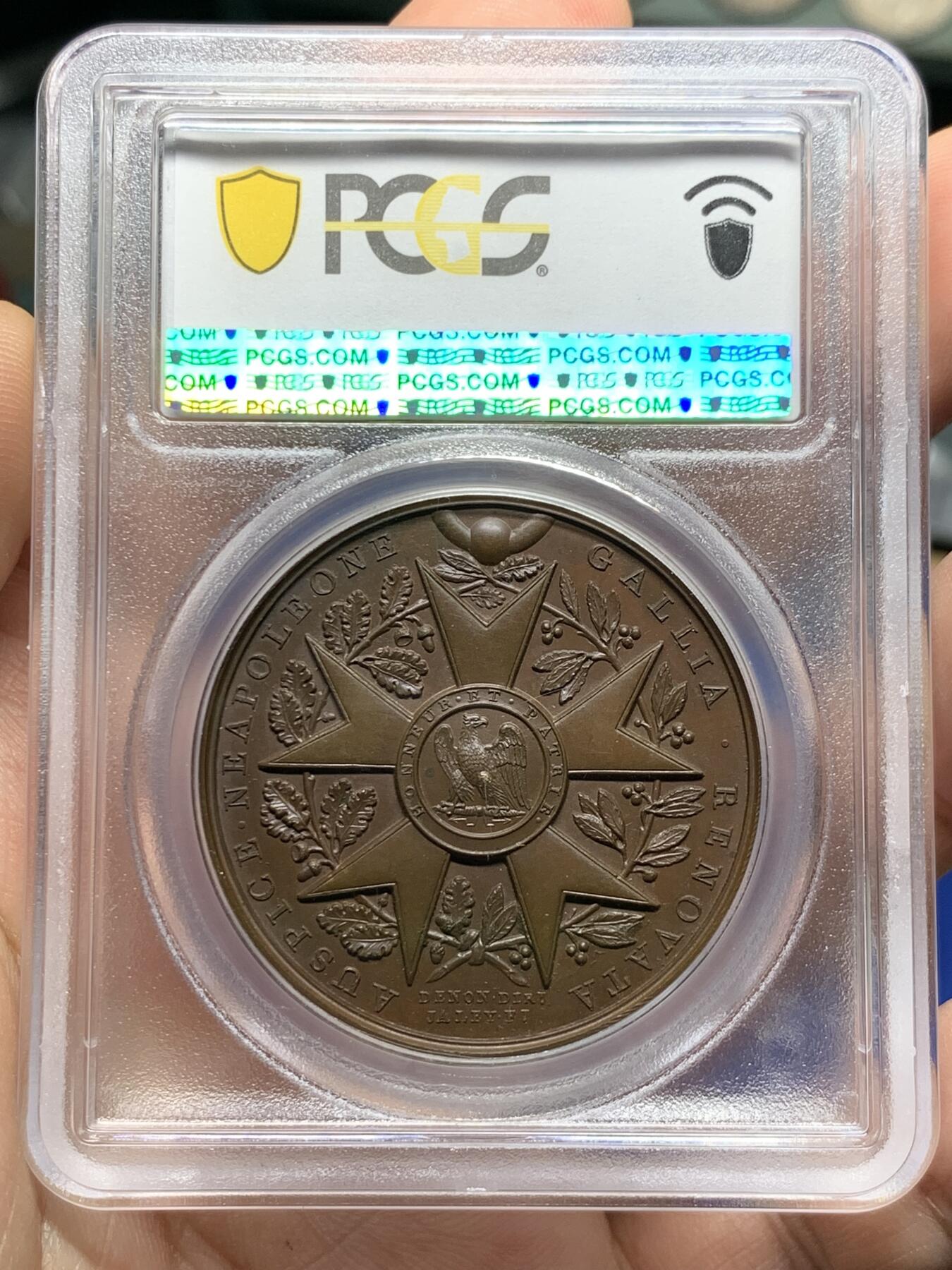 《竞宝斋》第387场 周日，周一 2场连拍 （全场包邮） PCGS SP65 冠军分 法国1804年拿破仑荣誉军团原铸铜章 巴黎造币厂巧克力包浆 荣誉军团勋章交织在月桂树和橡树花环间 ，创造性地将这样一枚传奇的勋章呈现于铜章之上，创意十足远超时代，上部佩环，中间是拿破仑鹰徽和该勋章的铭文 Honneur et Patrie（“荣誉和祖国”），是法国最高的功绩勋章，由拿破仑本人于1802年创立，高浮雕品相顶级 ，属于拿章中的稀少名誉品种。加厚盒。