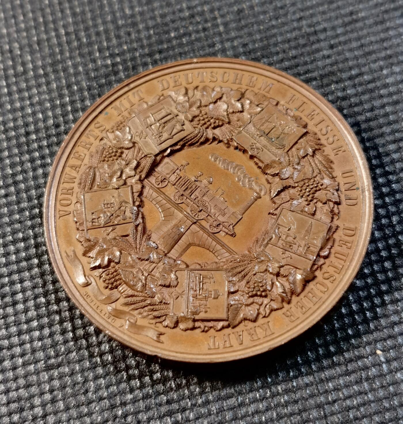  甄臻铺-世界币章拍卖（第24期），送拍享返佣金等优惠多多 1844年德国柏林工业博览会纪念铜章，正面是德意志女神Germania的半身像，背面展示工业成就场景，包括蒸汽机车和其他工业设备。由德国雕刻家创作，直径45毫米，重53.89克。铜质精良，雕工细腻，历史意义重大。正面德文铭文完整，背面环绕工业主题装饰纹样，体现了当时德国工业发展的繁荣景象