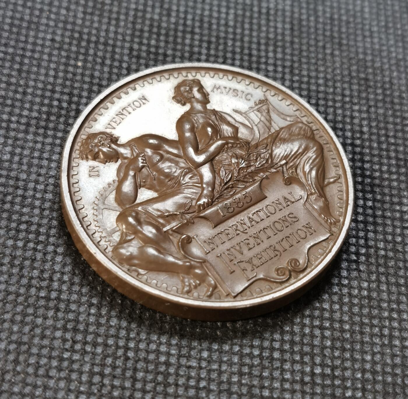  甄臻铺-世界币章拍卖（第24期），送拍享返佣金等优惠多多 1885年英国国际发明博览会纪念铜章，维多利亚女王授权，L.C.Wyon设计。正面是维多利亚女王侧面头像，背面是音乐和发明主题图案，工艺精美。直径45.5毫米，重51.89克，铜质材料。背面刻有