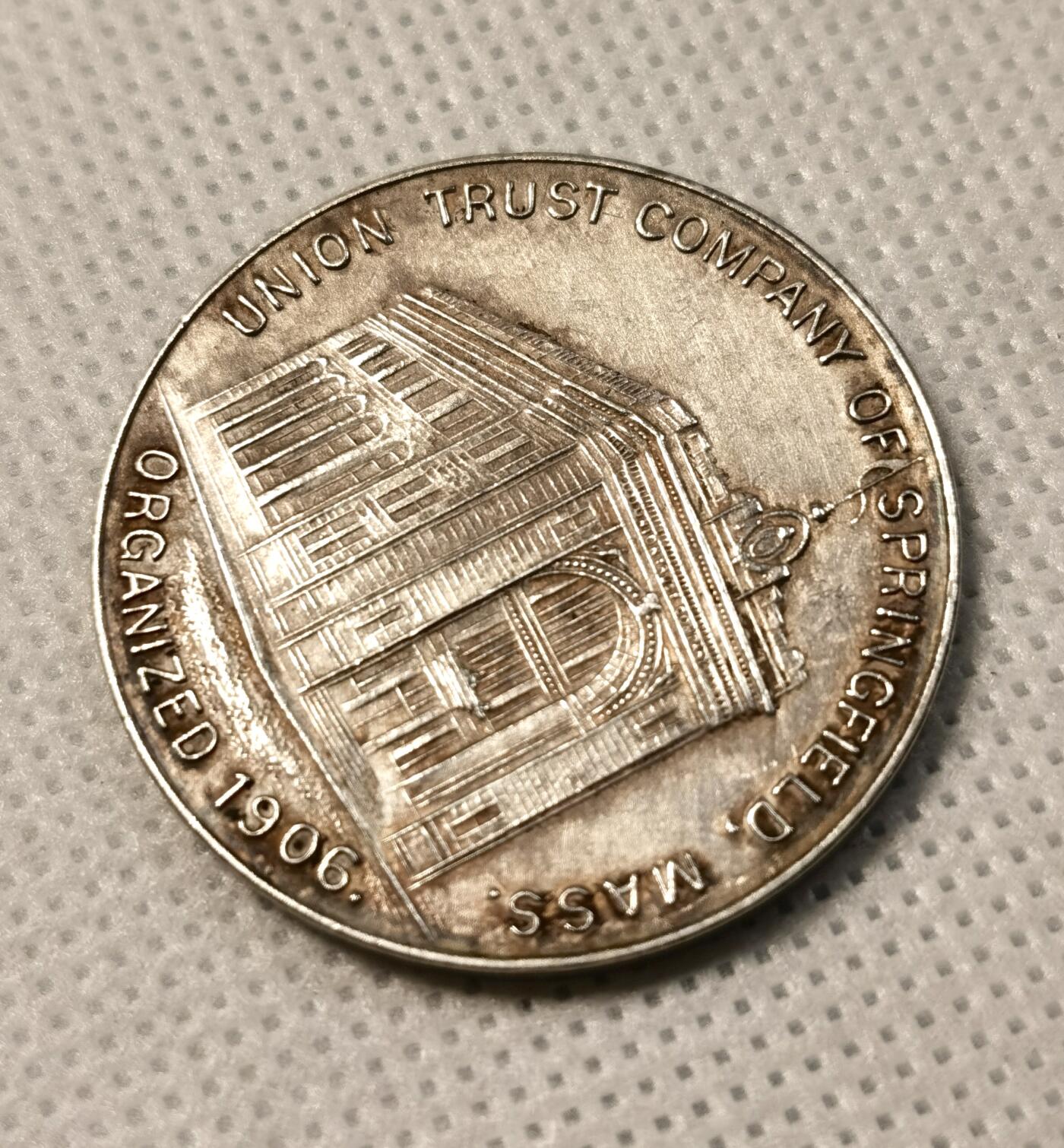  甄臻铺-世界币章拍卖（第25期），送拍享返佣金等优惠多多 美国Springfield Union Trust Company安全存款库纪念镀银铜章，直径32毫米，重14.1克。正面是公司大楼浮雕图案，背面刻有公司名称、资本额50万美元、盈余30万美元、安全存款库官员名单等信息。1906年公司成立时发行，包浆自然，稀少品种。