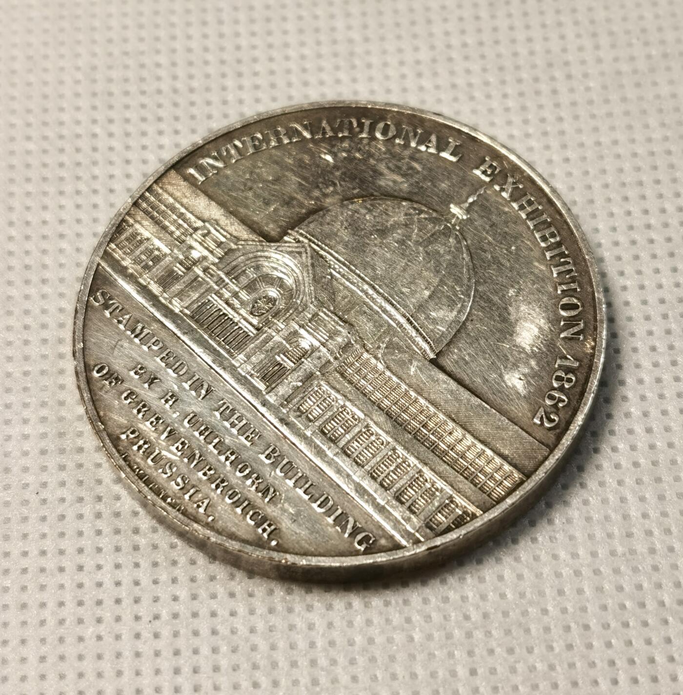 甄臻铺-世界币章拍卖（第25期），送拍享返佣金等优惠多多 1862年英国伦敦万国博览会纪念镀银铜章，正面刻有博览会建筑外景，背面是内部结构，由德国铸币师H. Uhlhorn制作。直径41.2毫米，重量36.8克。正面刻有
