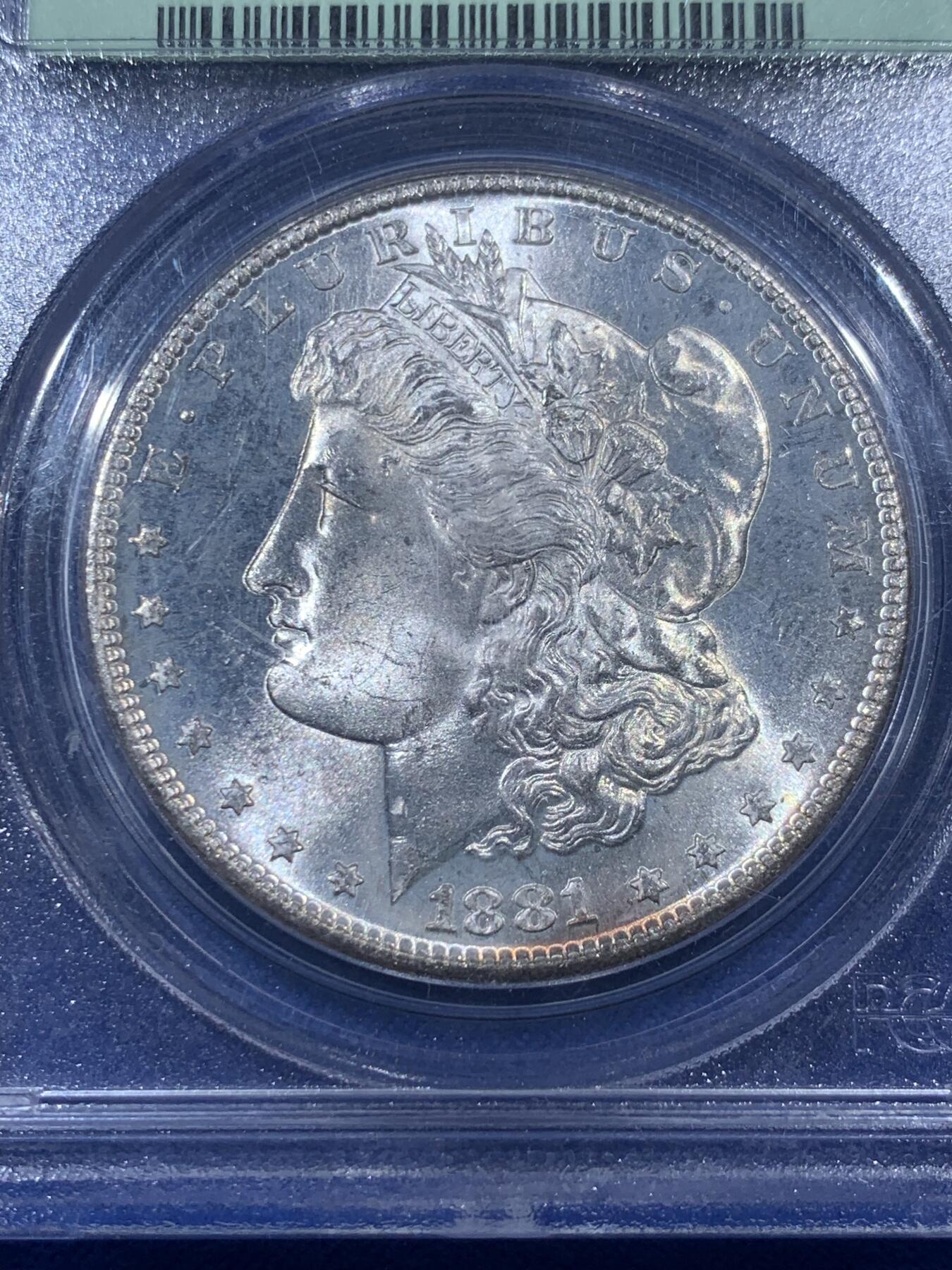 《竞宝斋》第405场 周日，周一，2场连拍 （全场包邮） PCGS MS65 美国1881年S版摩根1美元银币 人面打制完整 光感一流 鹰面超大月牙五彩包浆 由外向内光彩各异 堪称一绝 月牙彩是很受摩根玩家追捧的包浆之一 此枚更是大面积 高分数 深绿色渐变为粉色 十分难得 不容错过