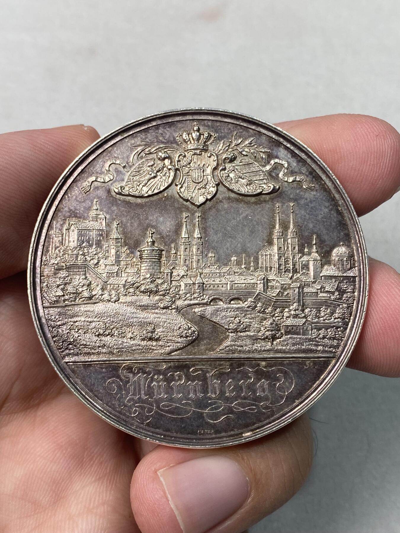 万国钱币拍卖第051期 1886年德国纽伦堡纪念银章，纪念普鲁士国王威廉二世访问，正面是纽伦堡城市全景浮雕，背面刻有威廉二世亲王访德日期1886年9月7-8日，银章极少见。重49.2克，直径50.4毫米，正反面原味底板氧化均匀呈紫罗兰五彩，边铭带990银标。