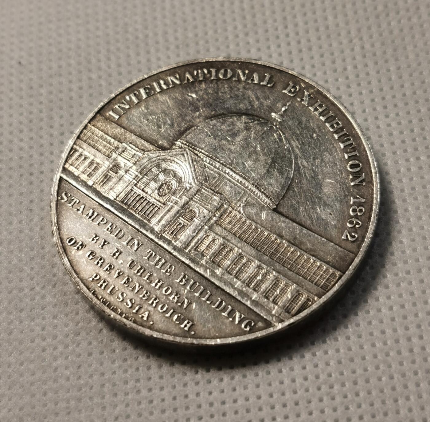 甄臻铺-世界币章拍卖（第30期），送拍享返佣金等优惠多多 1862年英国伦敦万国博览会纪念镀银铜章，正面刻有博览会建筑外景，背面是内部结构，由德国铸币师H. Uhlhorn制作。直径41.2毫米，重量36.8克。正面刻有
