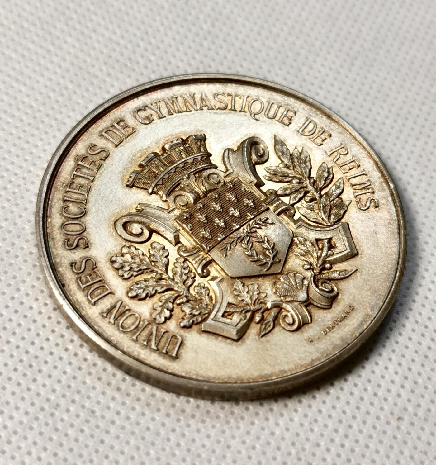 甄臻铺-世界币章拍卖（第30期），送拍享返佣金等优惠多多 1887年法国里尔体操协会颁发的鎏金银章，正面刻有皇冠和盾形纹章，周围环绕橄榄枝装饰。背面刻有