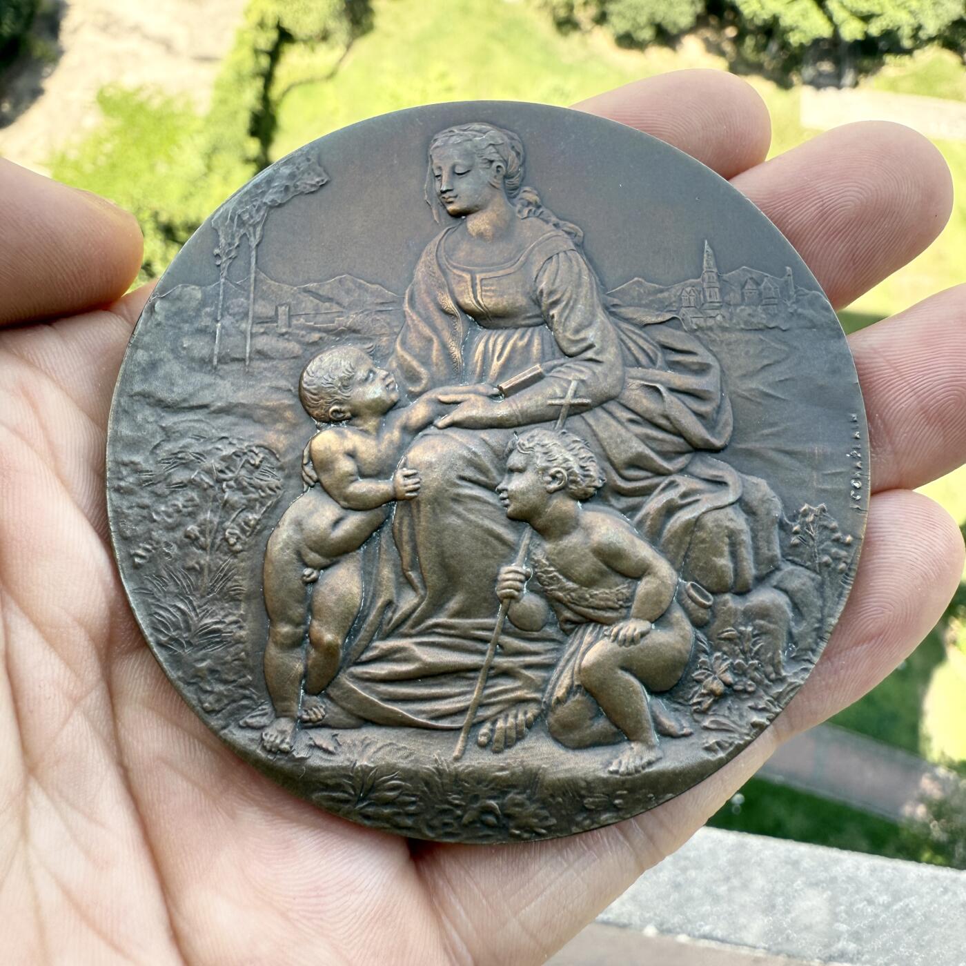 「木头集藏」章牌精品专场！ J. C. Chaplain～法国 花园中的圣母 大铜章，直径：68 mm，136 g，边铭：丰饶角 BRONZE，巴黎造币厂铸造。 此章正面图案取材于意大利画家拉斐尔·桑西于1507年到1508年间创作的油画《花园中的圣母》，是拉斐尔所作的圣母子像中的名作，现收藏于法国巴黎卢浮宫。在这幅圣母子像中，圣母爱抚着圣婴，小约翰手持木质十字架，整幅画面充满了温馨和慈爱。