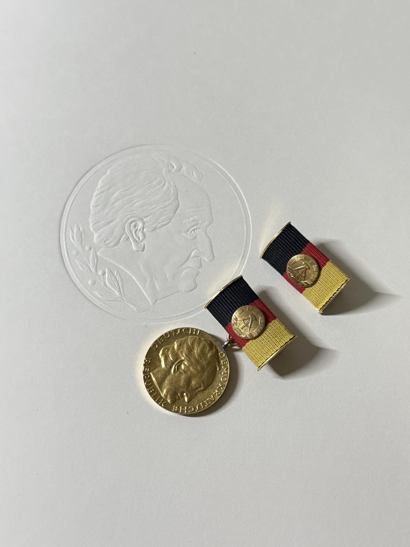 戎马世界章牌大赏第103期 东德歌德奖金（国家奖金）证章，带大证书，授予Hans Bekurts，得主介绍见最后一图，证书尺寸巨大仿皮非常厚实，实发非常少见，该证书为两德统一前最后一次授予的国家奖金，见证了东德的落幕