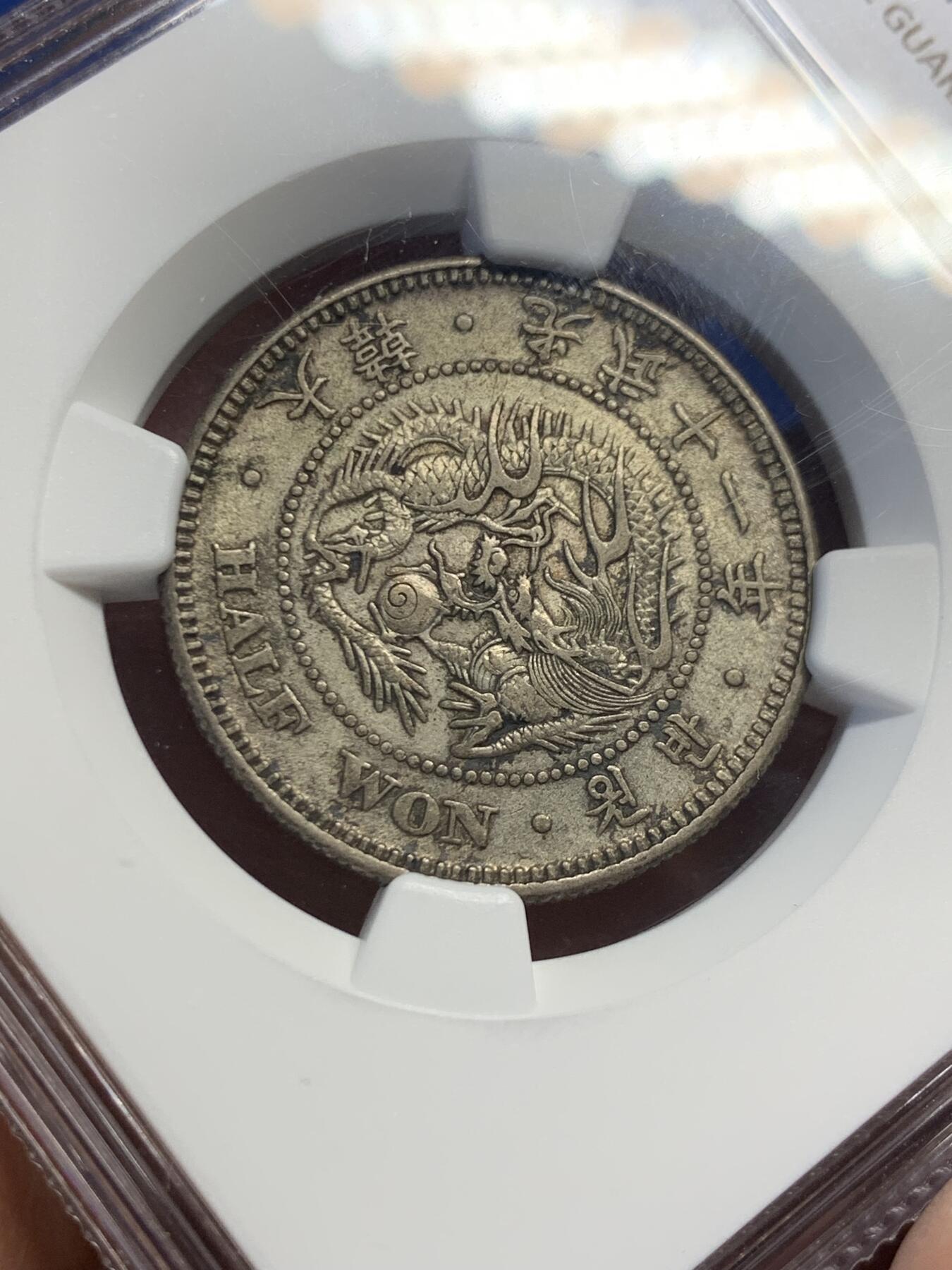 《竞宝斋》第415场 周日，周一，2场连拍 （全场包邮） NGC AU53  朝鲜1907年光武十一年半圆 小版稀少年份 黑金自然老彩，正面蟠龙戏珠图，龙身盘踞如环，背面上方为“李花章”（五瓣木槿花），下方交叉的桔梗花（左）与李花（右），低评状态，舒服怡人