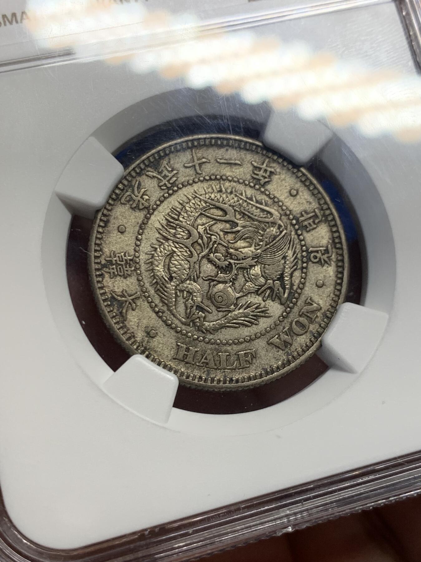 《竞宝斋》第415场 周日，周一，2场连拍 （全场包邮） NGC AU53  朝鲜1907年光武十一年半圆 小版稀少年份 黑金自然老彩，正面蟠龙戏珠图，龙身盘踞如环，背面上方为“李花章”（五瓣木槿花），下方交叉的桔梗花（左）与李花（右），低评状态，舒服怡人