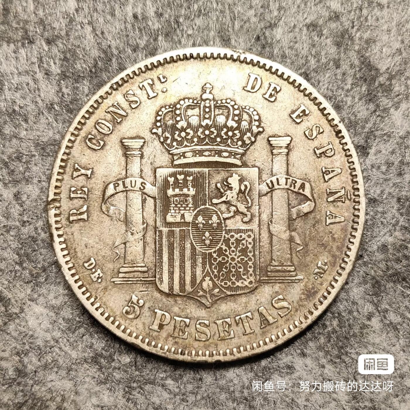 西班牙1877年阿方索十二世双柱5比塞塔银币 青年版少见。银币重25g，含银量90%。正面是西班牙国王阿方索十二世青年肖像，外环为拉丁文铭（阿方索十二世蒙神之恩）。背面图案是西班牙盾徽，盾徽中间椭圆内有三朵鸢尾花代表波旁王朝家族，椭圆旁有4栏分别代表四个王国。两侧各列一根海格力斯柱柱上卷轴绕裹，卷轴上有“海外有大陆”。头发细节全酱彩包浆，稀少版别流通好品。售出不退不换菜鸟包邮