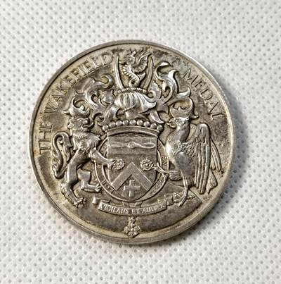 甄臻铺-世界币章拍卖（第35期），送拍享返佣金等优惠多多 - The Wakefield Medal 1938年英国殖民地海外比赛纪念银章，正面是狮子和鹰的浮雕图案，中间是盾形徽章，背面刻有NRA BRITISH COLONIES AND PROTECTORATES OVERSEAS MATCH字样。直径41.3毫米，重43.3克，边缘刻有获奖者及日期字样