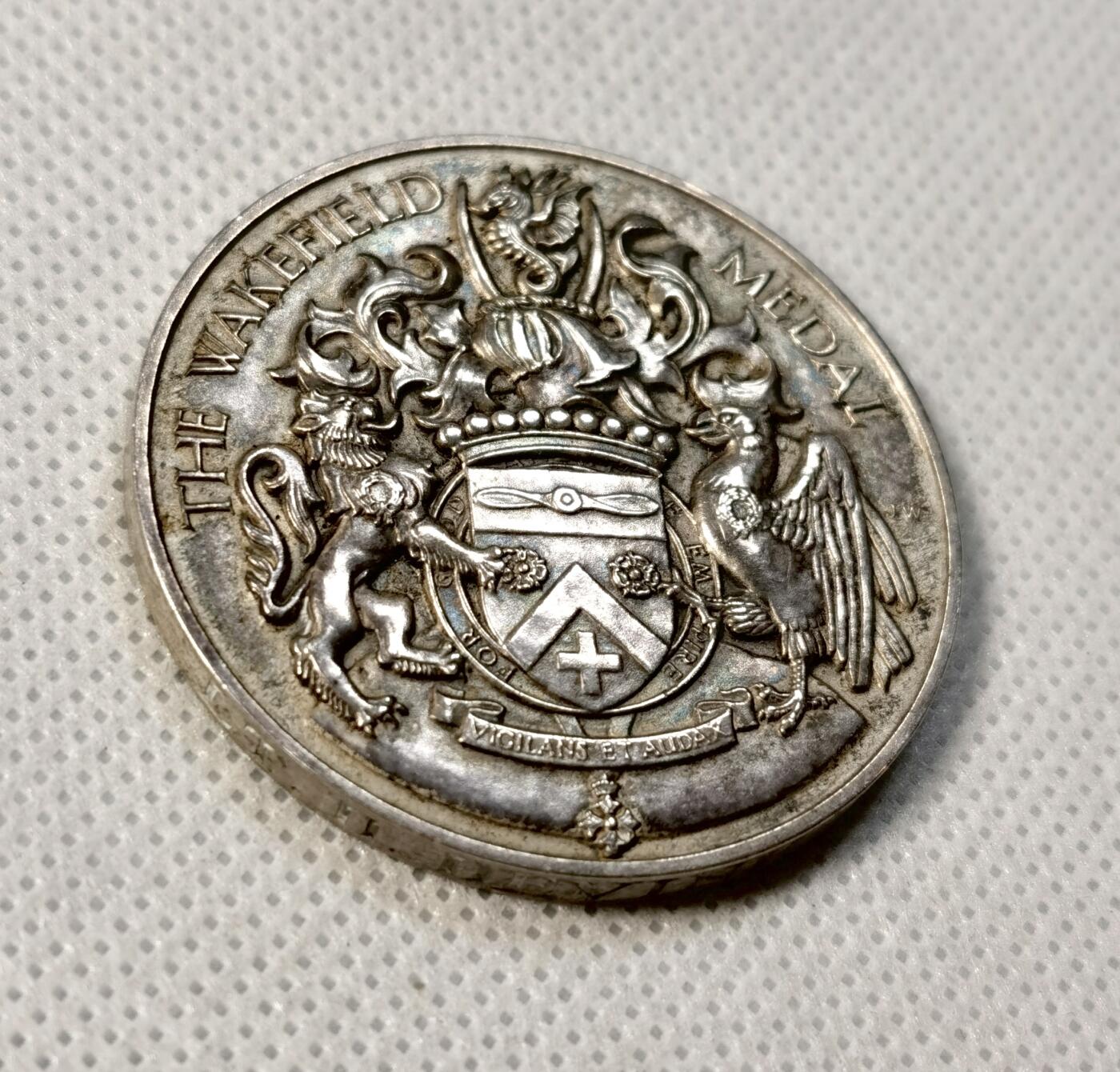 甄臻铺-世界币章拍卖（第35期），送拍享返佣金等优惠多多 The Wakefield Medal 1938年英国殖民地海外比赛纪念银章，正面是狮子和鹰的浮雕图案，中间是盾形徽章，背面刻有NRA BRITISH COLONIES AND PROTECTORATES OVERSEAS MATCH字样。直径41.3毫米，重43.3克，边缘刻有获奖者及日期字样