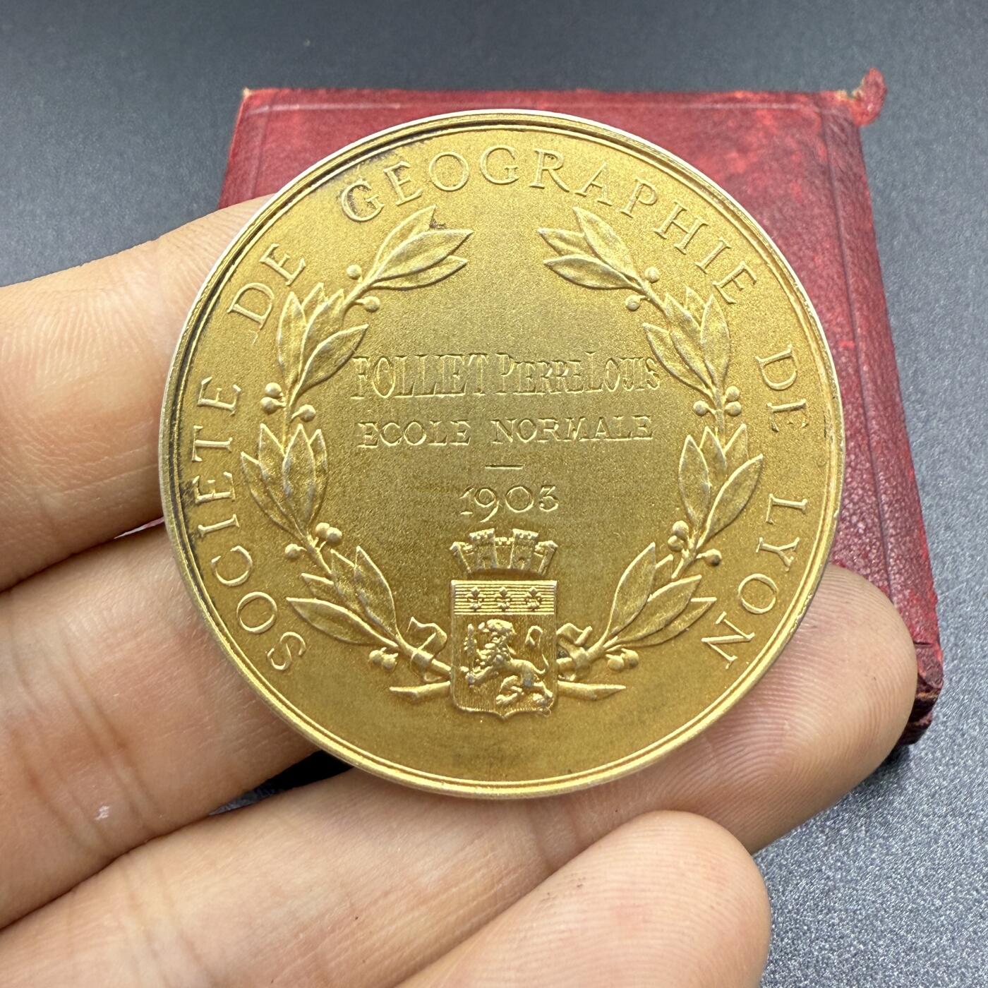 「木头集藏」“双节献礼”——章牌精品专场！ 1903年法国里昂地理学会镀金原盒银章，直径：41 mm，31.8 g，正面刻画玛丽安娜女神高举火炬照亮基座上地球仪，基座上的“PAX”（和平）铭牌、双蛇杖（商业与医学的象征）、矛（殖民与战争）、帆船（航海）、植物（丰收）等元素，寓意地理对各项工作的重要性；背面刻画里昂城市盾徽。很少见的一款银章，品相不错！