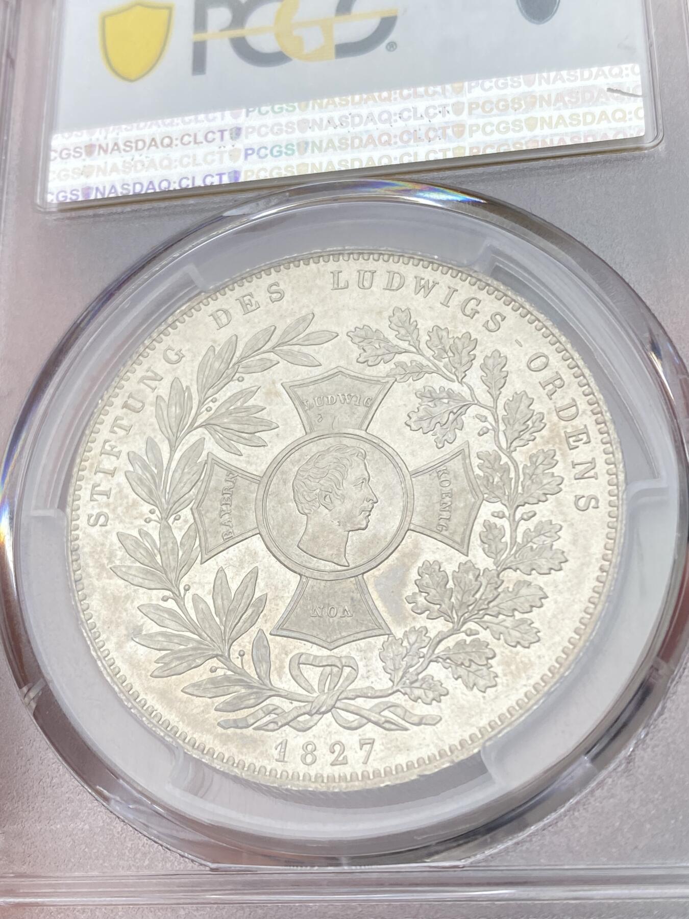 万国钱币拍卖第054期 PCGS MS65 1827巴伐利亚路德维希勋章历史泰勒 1827年8月25日，路德维希一世以国王之名设立了路德维希勋章，用以表彰为王国服务满50周年的杰出人员，并敕令造币厂发行此历史泰勒加以纪念。系列中的罕见品种，BU级别更是难得一见，丝绸地板黄油转光。（评级盒背面左上缺角）