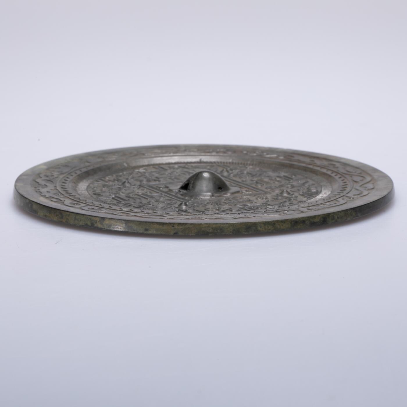 日本大阪雅和auction 2025金秋競賣會第一期 漢 走獸紋規矩鏡 尺寸:D:14cm 備註:盒付   此面漢代走獸紋規矩鏡，鏡體渾圓厚重，通體黑漆古包漿，色澤沉潤柔和，鏡背以精細線條鑄出走獸紋飾，或奔或躍，神態生動，間以幾何規矩紋相間佈局，構圖嚴謹而富節奏感。鏡紐高起，形制端正，邊廓勻整，展現漢代青銅鏡工藝的成熟與規範之美。此類鏡多寓意驅邪護身、吉祥長安，包漿溫潤，光澤深邃，鏡面保存完好，實屬難得。其兼具實用與審美價值，彰顯漢代金屬藝術的莊重典