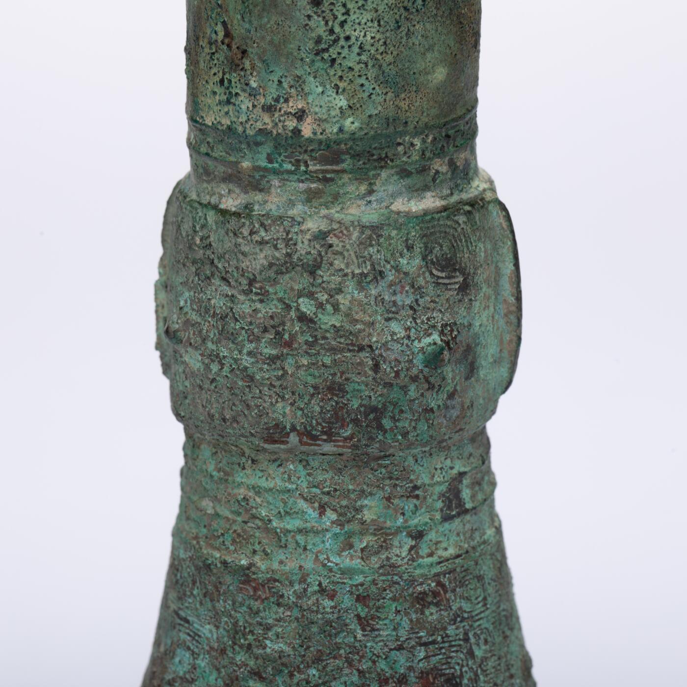 日本大阪雅和auction 2025金秋競賣會第一期 商 饕餮紋花觚 尺寸:W:14.5 H:25.5cm 備註:商代饕餮紋花觚，通體造型高峻挺拔，線條勻稱流暢，腹部微鼓，頸部修長，口沿外撇，圈足穩健。全器以精緻的饕餮紋為主紋，繁而不亂，層次分明，展現出商代青銅藝術的莊嚴與神祕。花紋間飾以雷紋、夔龍及細密的幾何紋飾，刀痕遒勁，鑄工嚴謹。整器包漿古潤，青銅色澤沉靜雅緻，氣韻雄渾，威嚴中蘊含典雅之美。此觚不僅為祭祀禮器之代表，亦體現了商人敬天重禮的信仰與