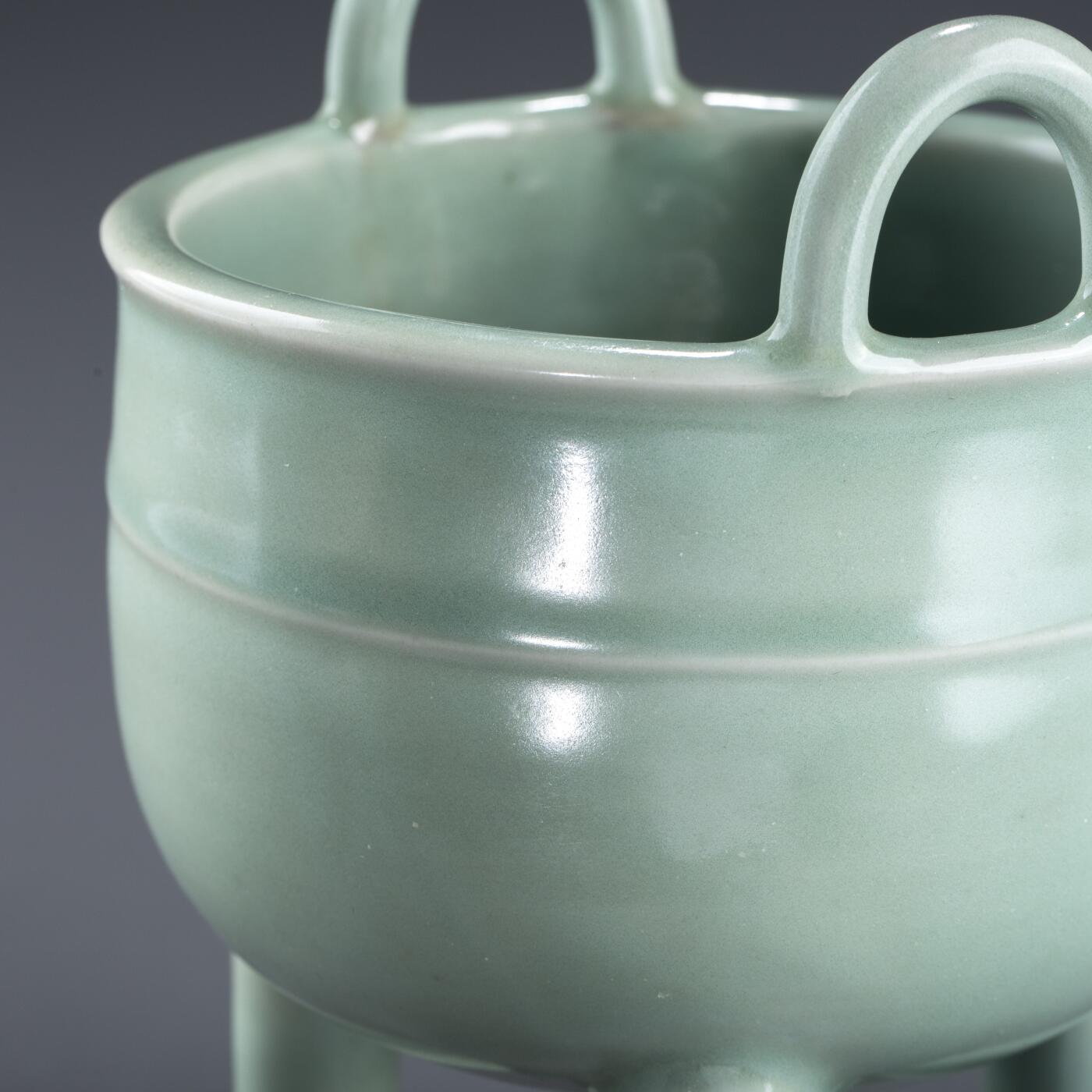 日本大阪雅和auction 2025金秋競賣會第一期 南宋 龍泉窯葱管三足鼎 尺寸:W:13 H:20cm 備註:盒付   此件南宋龍泉窯青釉鼎式爐，通體施粉青釉，色澤清潤如玉，呈柔和青翠之調，光潔內斂，頗具玉質之美。爐身圓腹，雙耳高聳上揚，三足中空、形似蔥管，挺拔穩健。整體比例勻稱，線條簡潔流暢，盡顯宋代器物的典雅之風。此式承襲青銅禮鼎造型，融祭器莊嚴與文房雅玩於一體，既可焚香，又具觀賞之趣，充分體現宋人「以瓷擬玉」之審美理想與高潔意趣。