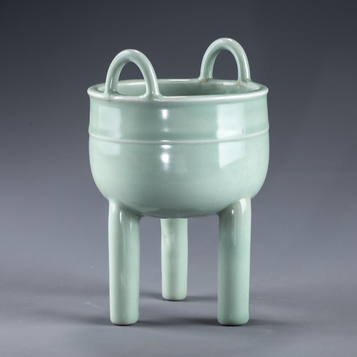 日本大阪雅和auction 2025金秋競賣會第一期 南宋 龍泉窯葱管三足鼎 尺寸:W:13 H:20cm 備註:盒付   此件南宋龍泉窯青釉鼎式爐，通體施粉青釉，色澤清潤如玉，呈柔和青翠之調，光潔內斂，頗具玉質之美。爐身圓腹，雙耳高聳上揚，三足中空、形似蔥管，挺拔穩健。整體比例勻稱，線條簡潔流暢，盡顯宋代器物的典雅之風。此式承襲青銅禮鼎造型，融祭器莊嚴與文房雅玩於一體，既可焚香，又具觀賞之趣，充分體現宋人「以瓷擬玉」之審美理想與高潔意趣。