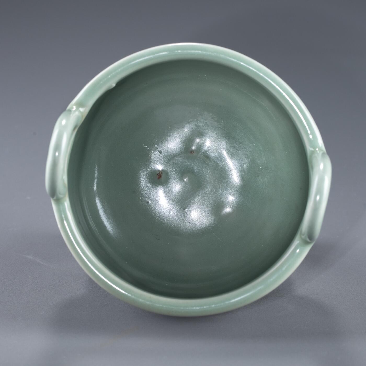 日本大阪雅和auction 2025金秋競賣會第一期 南宋 龍泉窯葱管三足鼎 尺寸:W:13 H:20cm 備註:盒付   此件南宋龍泉窯青釉鼎式爐，通體施粉青釉，色澤清潤如玉，呈柔和青翠之調，光潔內斂，頗具玉質之美。爐身圓腹，雙耳高聳上揚，三足中空、形似蔥管，挺拔穩健。整體比例勻稱，線條簡潔流暢，盡顯宋代器物的典雅之風。此式承襲青銅禮鼎造型，融祭器莊嚴與文房雅玩於一體，既可焚香，又具觀賞之趣，充分體現宋人「以瓷擬玉」之審美理想與高潔意趣。