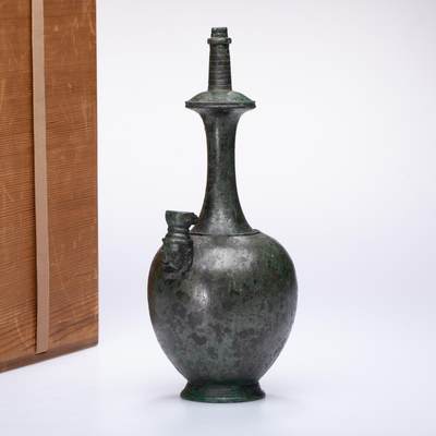 日本大阪雅和auction 2025金秋競賣會第一期 - 唐 青銅淨瓶 尺寸:W:11 H:25cm 備註:木箱   此件青銅淨瓶，器形修長，頸部細長挺拔，口沿微侈，下承渾圓飽滿之腹，造型端莊雅緻。瓶身青銅質地厚重，表面自然氧化生成古雅綠銹，顯現歲月沉積之美。側設流嘴，裝飾獸首紋飾，神態生動，富於盛唐金屬工藝的雄渾氣韻。淨瓶原為佛教供器，寓意「淨水清心」，常置於壇前或菩薩手中，以示清淨無垢。此器比例協調，鑄造精良，既具宗教意涵，又為唐代青銅藝術之典型代表