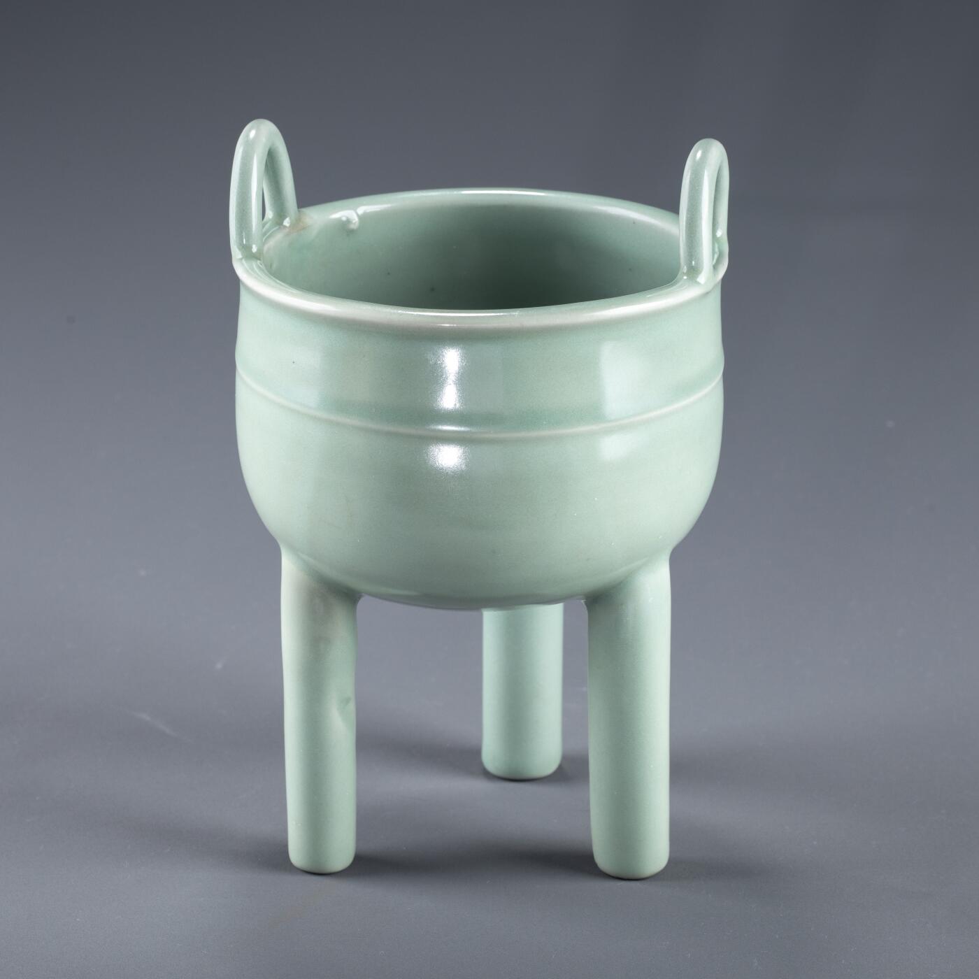 日本大阪雅和auction 2025金秋競賣會第一期 南宋 龍泉窯葱管三足鼎 尺寸:W:13 H:20cm 備註:盒付   此件南宋龍泉窯青釉鼎式爐，通體施粉青釉，色澤清潤如玉，呈柔和青翠之調，光潔內斂，頗具玉質之美。爐身圓腹，雙耳高聳上揚，三足中空、形似蔥管，挺拔穩健。整體比例勻稱，線條簡潔流暢，盡顯宋代器物的典雅之風。此式承襲青銅禮鼎造型，融祭器莊嚴與文房雅玩於一體，既可焚香，又具觀賞之趣，充分體現宋人「以瓷擬玉」之審美理想與高潔意趣。