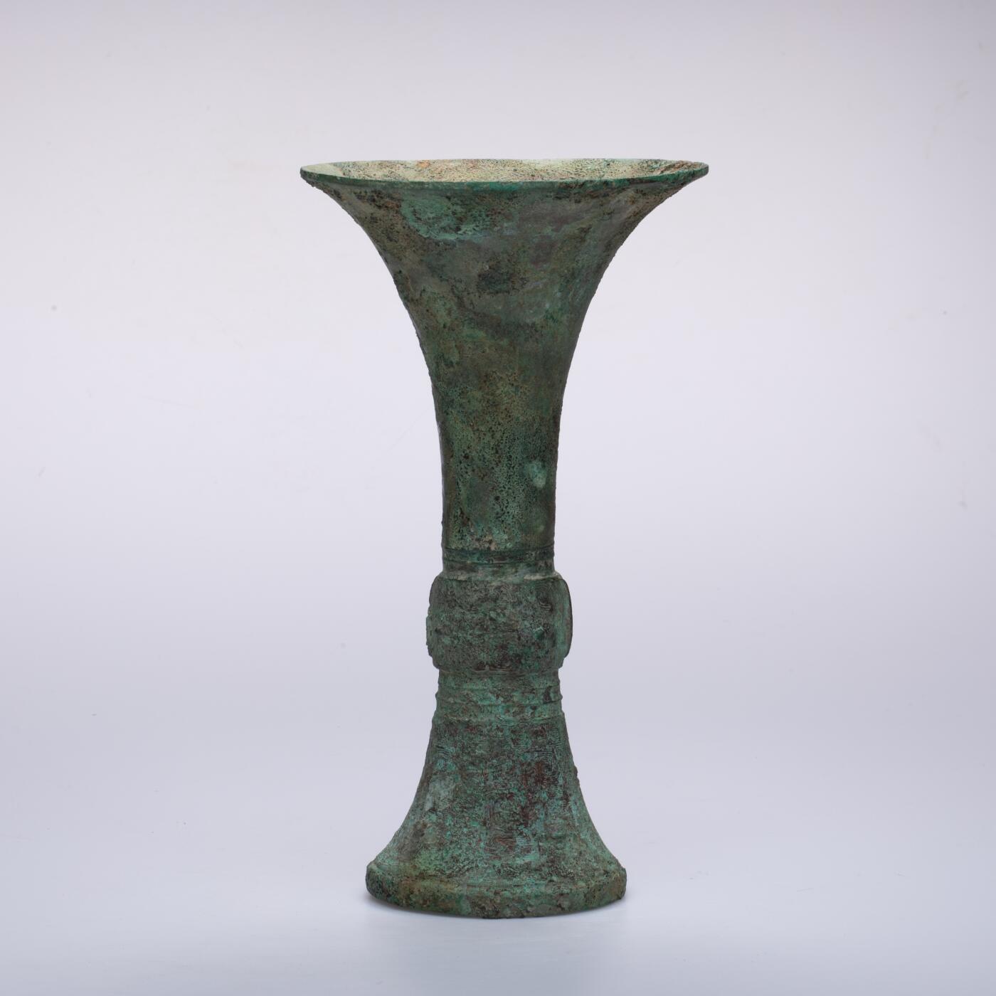 日本大阪雅和auction 2025金秋競賣會第一期 商 饕餮紋花觚 尺寸:W:14.5 H:25.5cm 備註:商代饕餮紋花觚，通體造型高峻挺拔，線條勻稱流暢，腹部微鼓，頸部修長，口沿外撇，圈足穩健。全器以精緻的饕餮紋為主紋，繁而不亂，層次分明，展現出商代青銅藝術的莊嚴與神祕。花紋間飾以雷紋、夔龍及細密的幾何紋飾，刀痕遒勁，鑄工嚴謹。整器包漿古潤，青銅色澤沉靜雅緻，氣韻雄渾，威嚴中蘊含典雅之美。此觚不僅為祭祀禮器之代表，亦體現了商人敬天重禮的信仰與