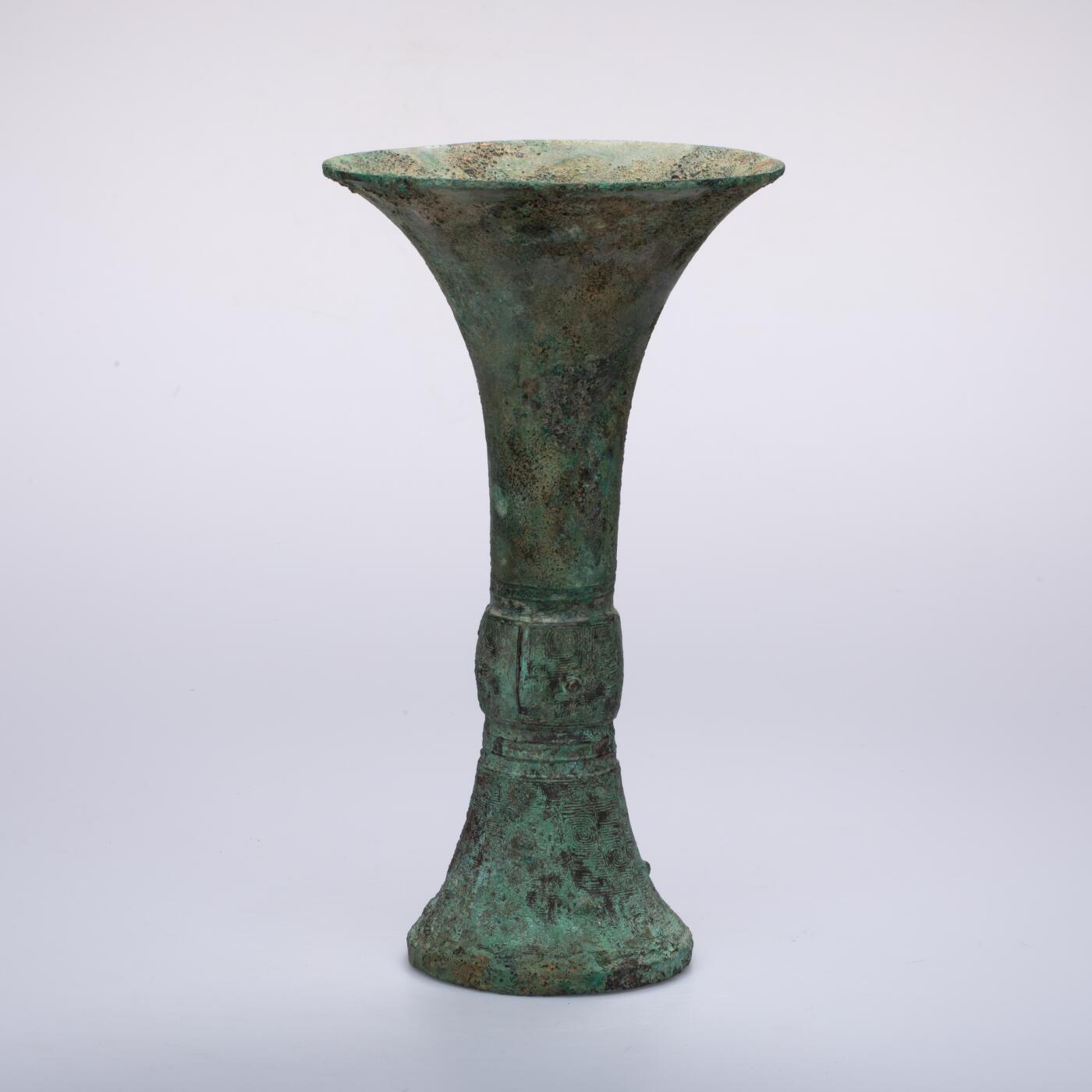 日本大阪雅和auction 2025金秋競賣會第一期 商 饕餮紋花觚 尺寸:W:14.5 H:25.5cm 備註:商代饕餮紋花觚，通體造型高峻挺拔，線條勻稱流暢，腹部微鼓，頸部修長，口沿外撇，圈足穩健。全器以精緻的饕餮紋為主紋，繁而不亂，層次分明，展現出商代青銅藝術的莊嚴與神祕。花紋間飾以雷紋、夔龍及細密的幾何紋飾，刀痕遒勁，鑄工嚴謹。整器包漿古潤，青銅色澤沉靜雅緻，氣韻雄渾，威嚴中蘊含典雅之美。此觚不僅為祭祀禮器之代表，亦體現了商人敬天重禮的信仰與