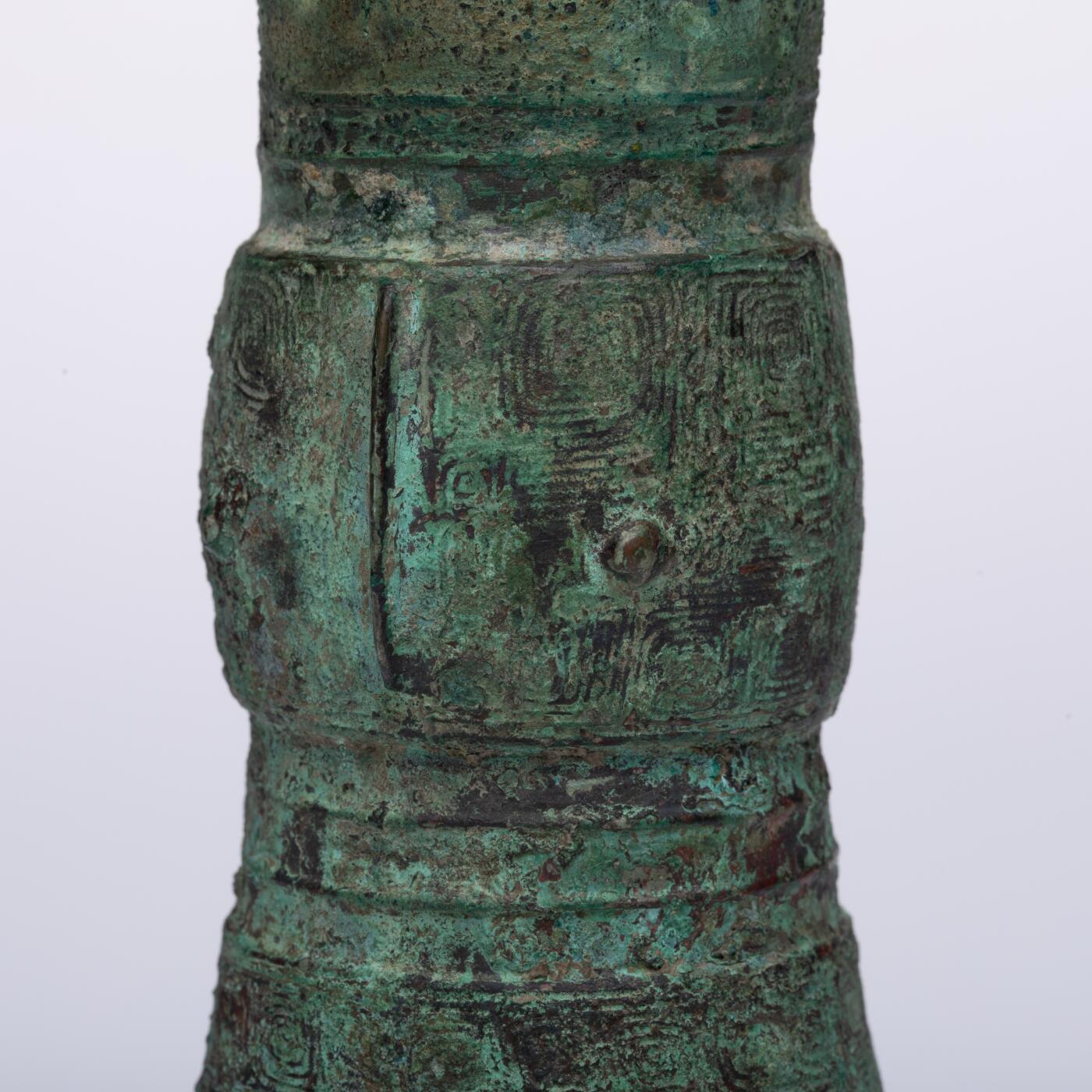 日本大阪雅和auction 2025金秋競賣會第一期 商 饕餮紋花觚 尺寸:W:14.5 H:25.5cm 備註:商代饕餮紋花觚，通體造型高峻挺拔，線條勻稱流暢，腹部微鼓，頸部修長，口沿外撇，圈足穩健。全器以精緻的饕餮紋為主紋，繁而不亂，層次分明，展現出商代青銅藝術的莊嚴與神祕。花紋間飾以雷紋、夔龍及細密的幾何紋飾，刀痕遒勁，鑄工嚴謹。整器包漿古潤，青銅色澤沉靜雅緻，氣韻雄渾，威嚴中蘊含典雅之美。此觚不僅為祭祀禮器之代表，亦體現了商人敬天重禮的信仰與