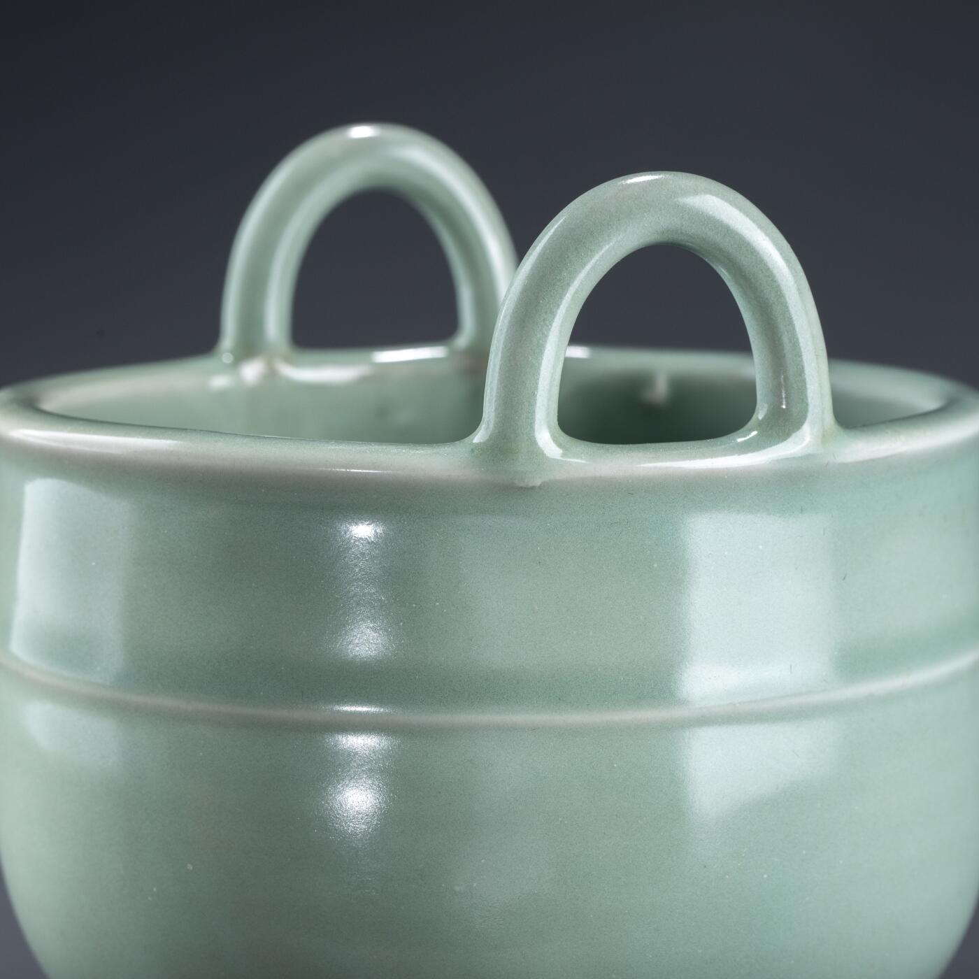 日本大阪雅和auction 2025金秋競賣會第一期 南宋 龍泉窯葱管三足鼎 尺寸:W:13 H:20cm 備註:盒付   此件南宋龍泉窯青釉鼎式爐，通體施粉青釉，色澤清潤如玉，呈柔和青翠之調，光潔內斂，頗具玉質之美。爐身圓腹，雙耳高聳上揚，三足中空、形似蔥管，挺拔穩健。整體比例勻稱，線條簡潔流暢，盡顯宋代器物的典雅之風。此式承襲青銅禮鼎造型，融祭器莊嚴與文房雅玩於一體，既可焚香，又具觀賞之趣，充分體現宋人「以瓷擬玉」之審美理想與高潔意趣。