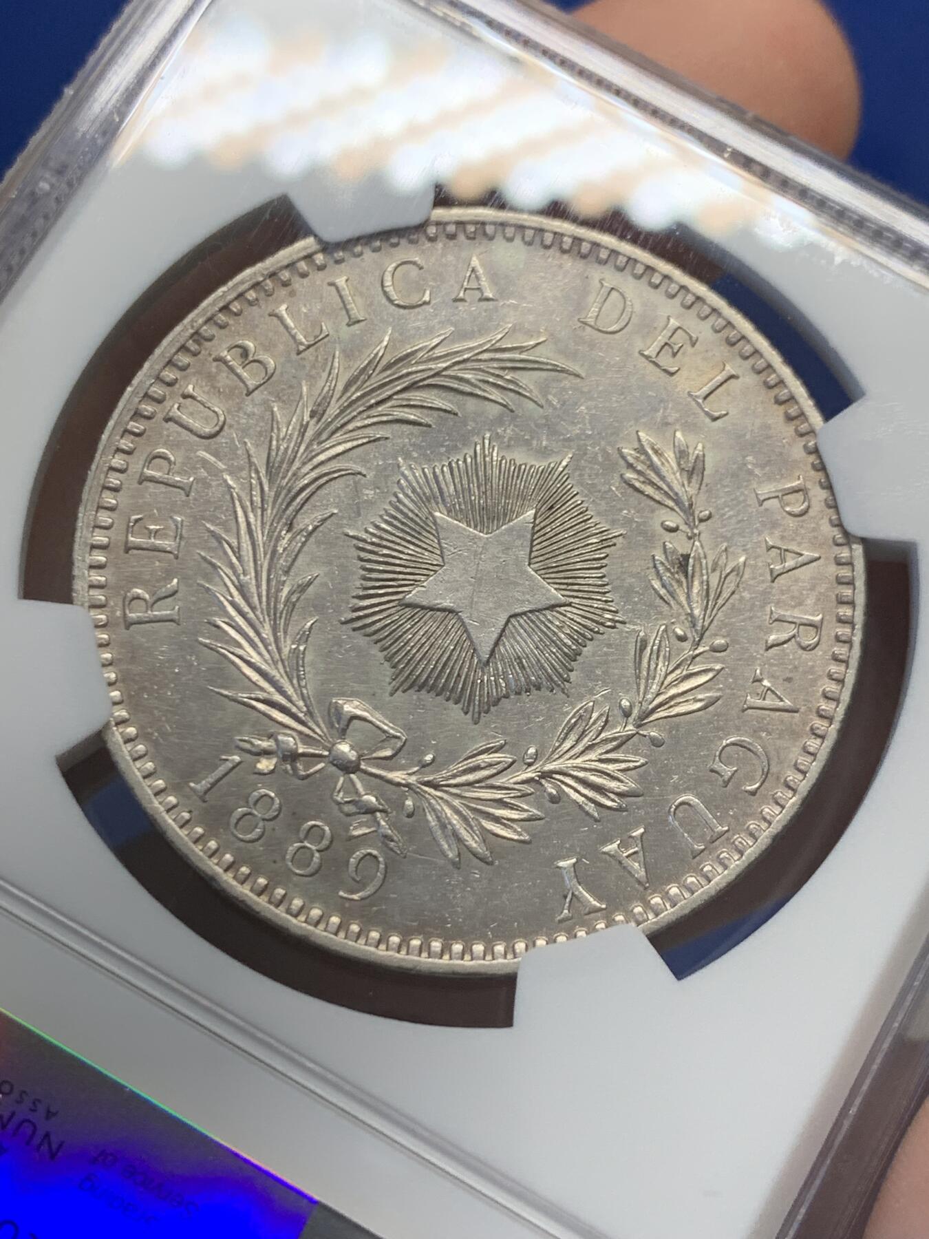 《竞宝斋》第436场 周日，周一2场连拍 （全场包邮） NGC UNCD 巴拉圭1889年雄狮1比索大银币，正面图为一头卷毛雄狮蹲坐守卫着自由之竿和自由之帽，反面图中间有一枚光芒四射的五角星，以此纪念1811年5月摆脱西班牙殖民统治获得独立。