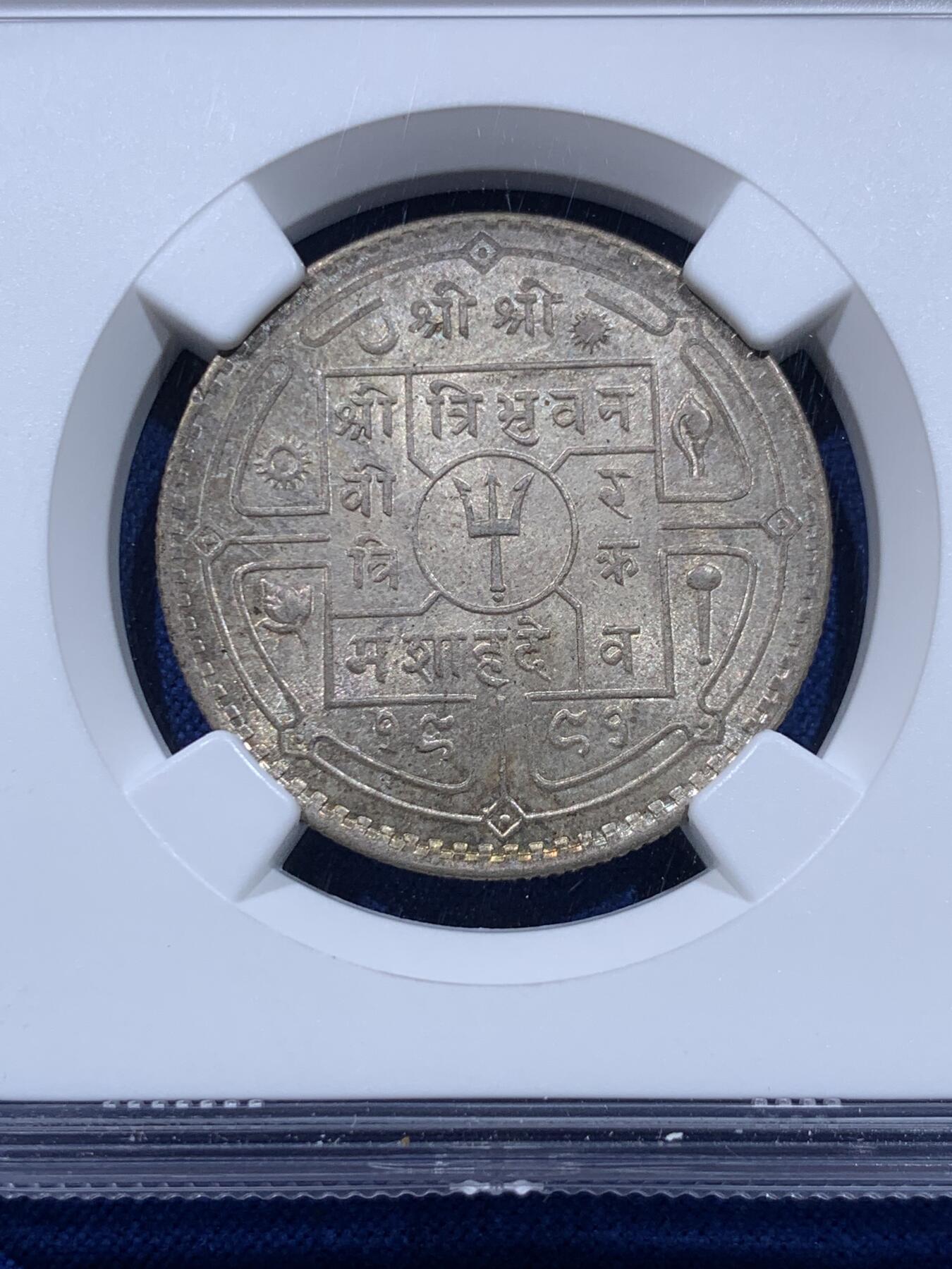 《竞宝斋》第437场 周日，周一2场连拍 （全场包邮） NGC MS64 尼泊尔1934年 1卢比银币。从美国老藏家币夹中拆出，有着长久存放产生的烟灰质感包浆，其6点钟方向有着一抹亮眼的金色月牙包浆，给整币画上点睛之笔，让平凡的品种有了非凡的观感。