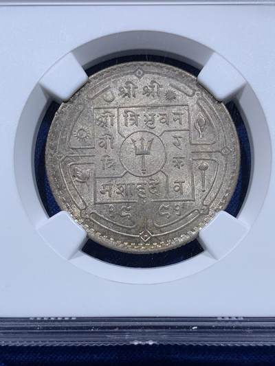 《竞宝斋》第437场 周日，周一2场连拍 （全场包邮） NGC MS64 尼泊尔1934年 1卢比银币。从美国老藏家币夹中拆出，有着长久存放产生的烟灰质感包浆，其6点钟方向有着一抹亮眼的金色月牙包浆，给整币画上点睛之笔，让平凡的品种有了非凡的观感。