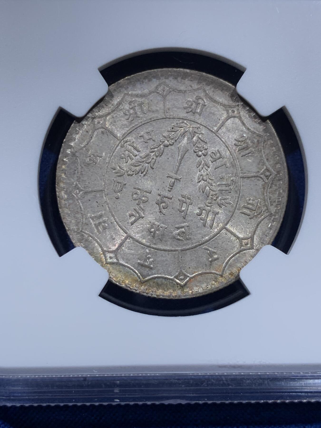 《竞宝斋》第437场 周日，周一2场连拍 （全场包邮） NGC MS64 尼泊尔1934年 1卢比银币。从美国老藏家币夹中拆出，有着长久存放产生的烟灰质感包浆，其6点钟方向有着一抹亮眼的金色月牙包浆，给整币画上点睛之笔，让平凡的品种有了非凡的观感。