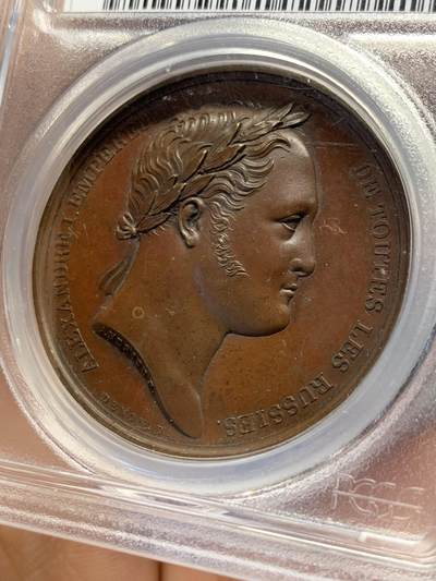 《竞宝斋》第438场 周日，周一，周二 3场连拍 （全场包邮） PCGS SP64 亚军分 法国1814年沙皇亚历山大一世访问巴黎铜章 正面沙皇月桂冠高浮雕，完全拿章典型风格头像，背面天使坐于树荫下书写历史，纪念沙皇占领期访巴黎造币厂，第六次反法同盟胜利，法兰西第一帝国覆灭，拿皇退位流放，巴黎由俄军掌管。作为胜利者的沙皇骑着白马率大军通过凯旋门，不知他是否满脑一年前拿皇攻占莫斯科场景，与其说“访问巴黎”，不如说彰显复仇拿皇的耀武扬威。
