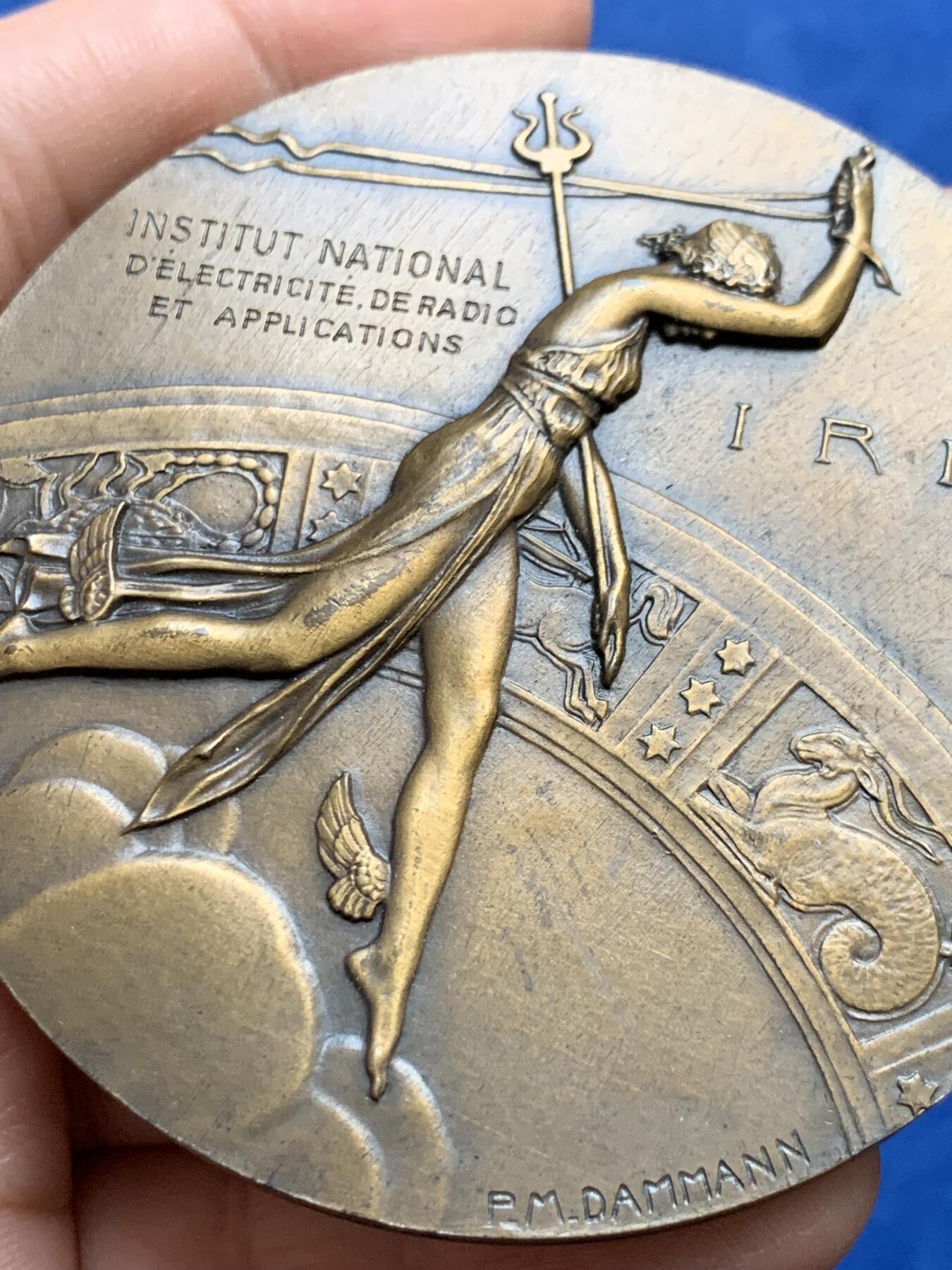 《竞宝斋》第438场 周日，周一，周二 3场连拍 （全场包邮） 名家DAMMANN作 1927年法国无线电报协会纪念大铜章 原铸  法国新艺术运动时期勋章艺术集珍 章牌编号：DAMMANN-1927-TSF   意象隐喻：彩虹女神伊里斯在希腊神话中司掌通信，其足踝双翼象征无远弗届的无线电波，科技符号：背面六边形天线网格暗合当时最先进的六角形蜂窝状信号塔设计，宇宙观表达：黄道带与星空的组合，暗示无线电技术突破时空界限的哲学意义。134.5克，67.5mm，丰饶角