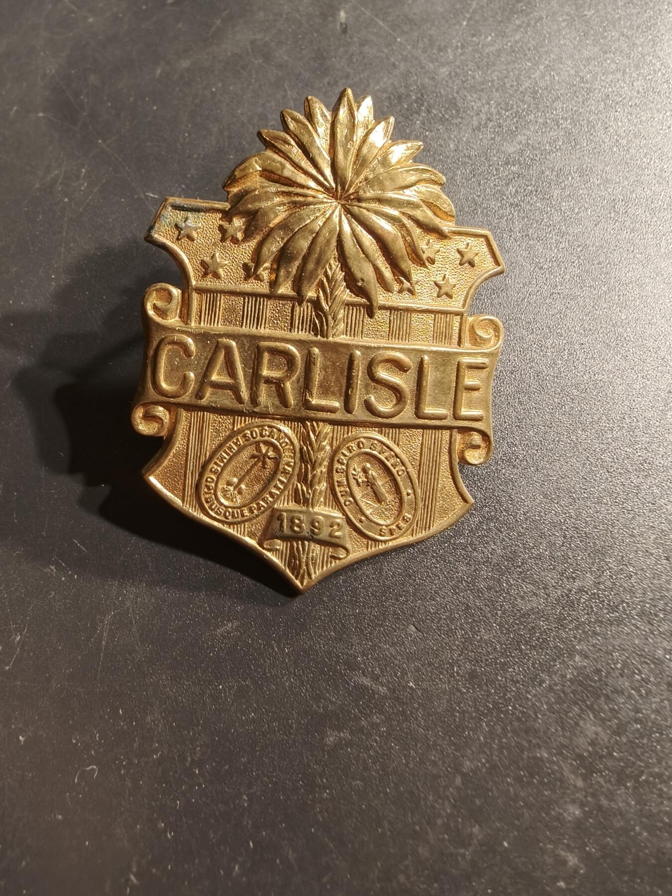 老王徽章第164期  美国卡莱尔印第安工业学校大檐帽徽      卡莱尔印第安工业学校由理查德·亨利·普拉特于1879年创立，是美国第一所联邦非保留地寄宿学校。学校的使命是“杀死印第安人，拯救人类”旨在通过教育和文化同化，将美洲原住民儿童融入白人社会。 该校运营了近40年，至1918年关闭 