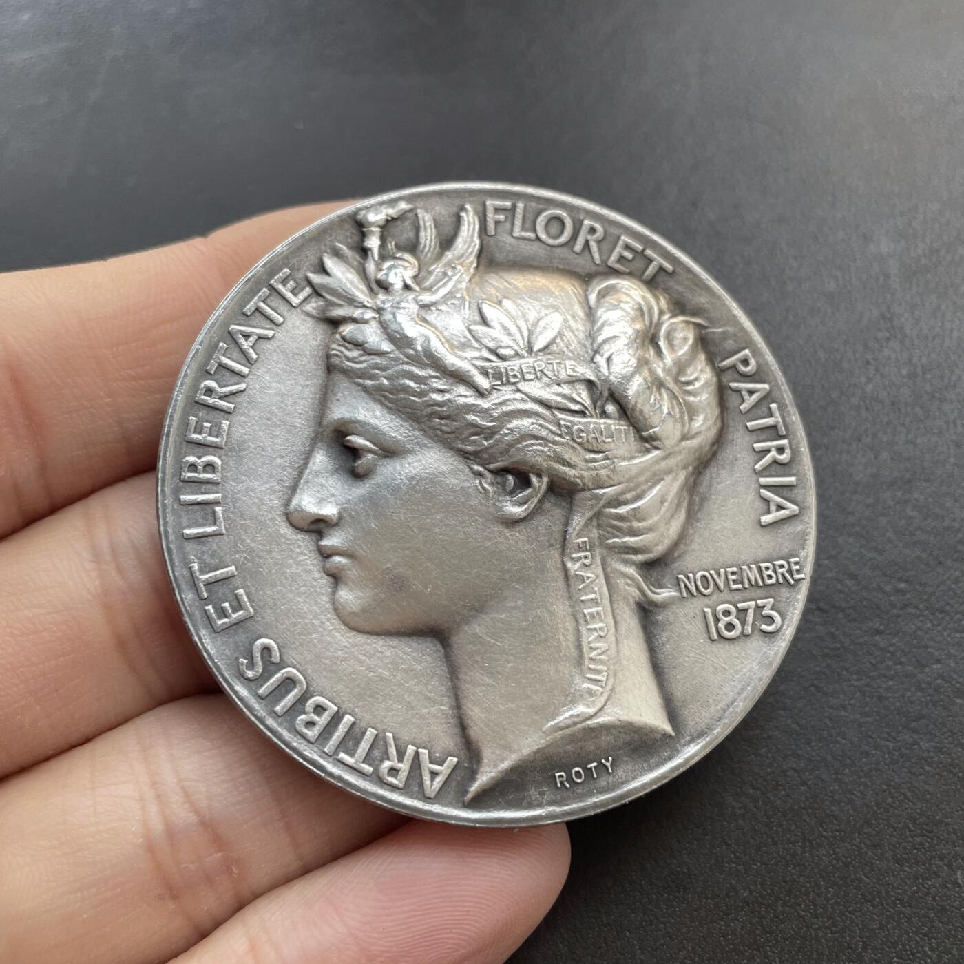 「木头集藏」章牌精品专场！ O Roty～法国烹饪协会宴会纪念镀银铜章 ，直径：51mm，边铭：丰饶角 BRONZE，正面的这款玛丽安娜肖像是罗蒂较早期的作品。章上的年份1873是烹饪协会成立的时间，并不是罗蒂创作这枚章的时间。罗蒂创作的时间大约在1880年代。  法国烹饪协会实际上是一个社交俱乐部，通过定期举办宴会，以表彰艺术、科学和政治领域的杰出人士，因此这个宴会就成为了一个名流云集的重要场合。