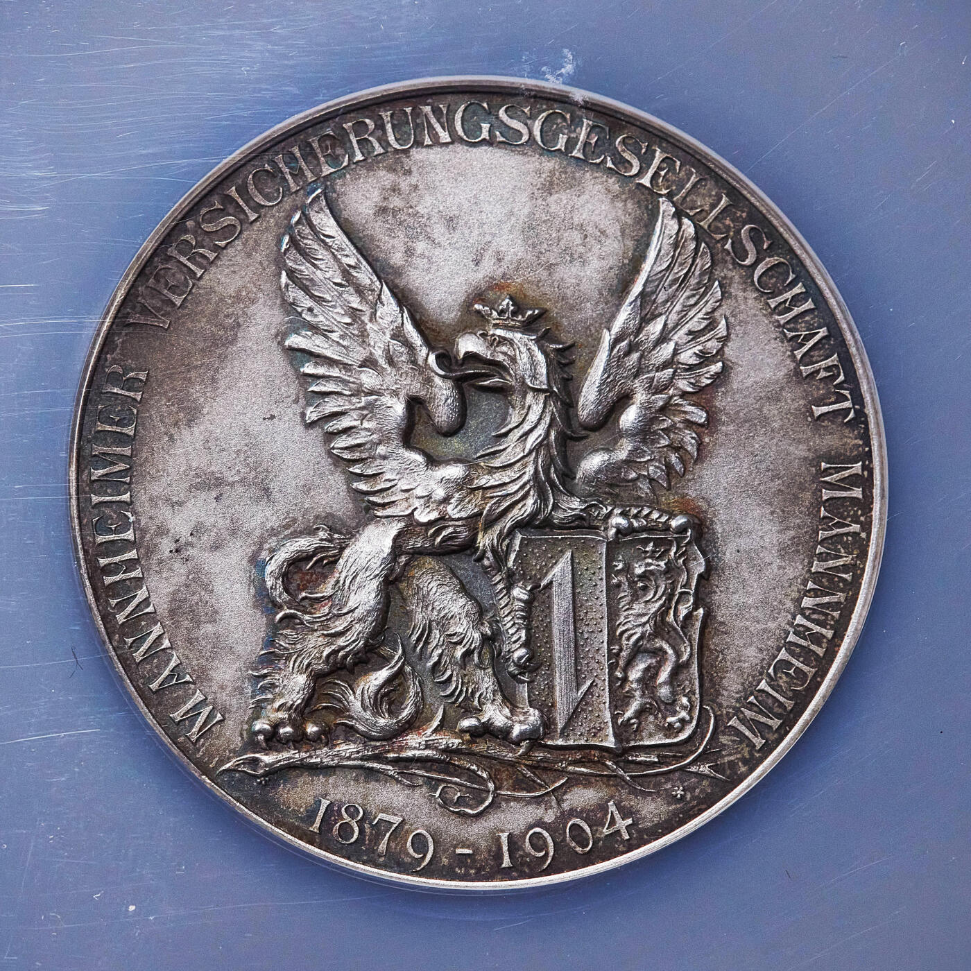 【俄甄集藏】2025年(045)12-03 星期三 晚 19:30 全场包邮 德国1904年纪念曼海姆保险公司成立25周年大银章，NGC MS63，直径：50mm，五彩老包浆，磨砂底板，正面展翼狮鹫为曼海姆市象征，背面蒸汽轮船为运输保险的基础业务，设计精美