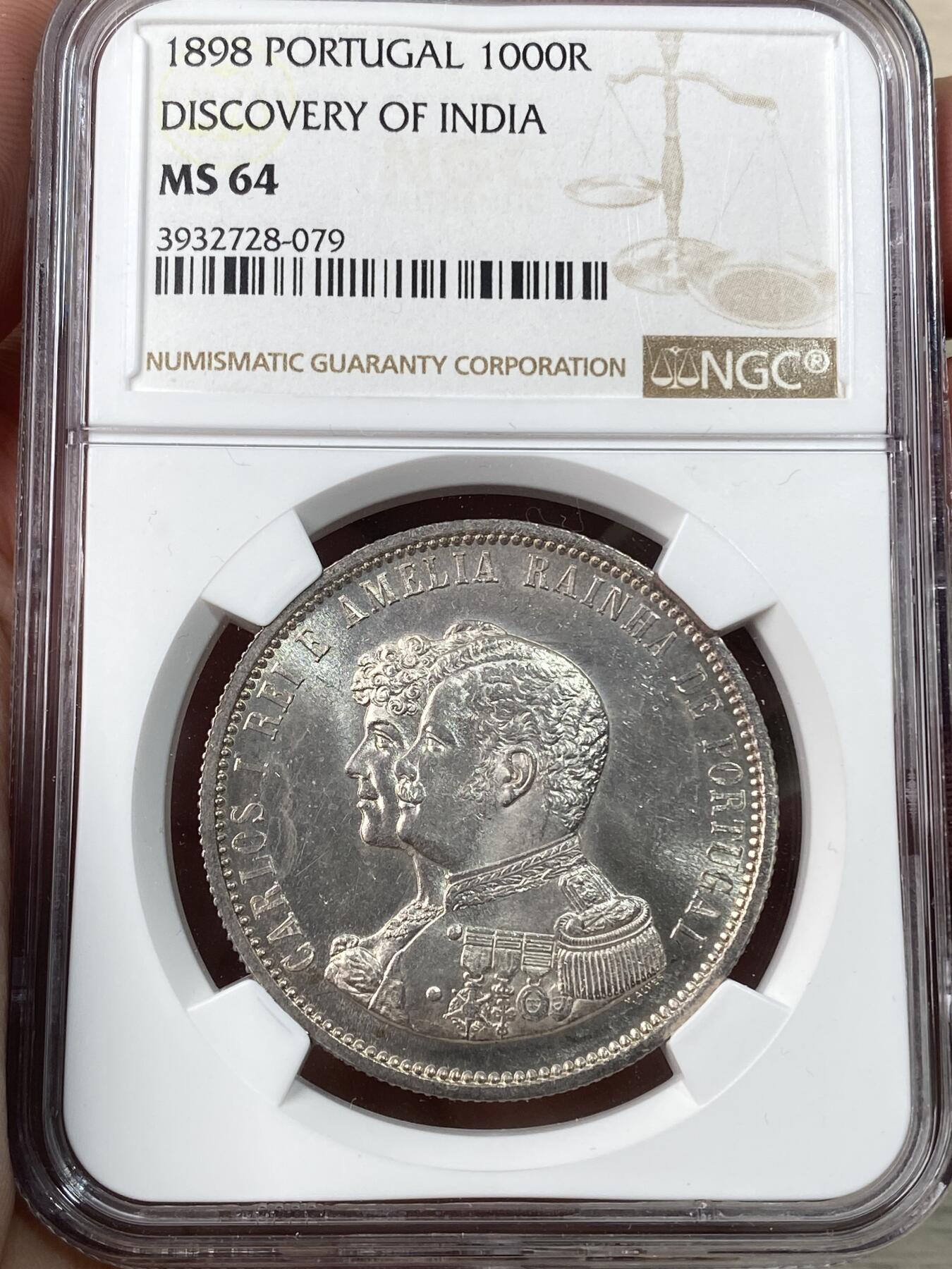 万国钱币拍卖第056期 NGC MS64  1898年葡萄牙1000雷亚尔大银币 纪念发现印度400周年 高分好状态 实物pl感 原银强霜光 打制优异 正面:葡萄牙国王卡洛斯一世和王后阿梅莉侧身半身像 背面:基督勋章十字架，四角有玫瑰花饰，周围有文字。此纪念币是为了纪念瓦斯科·达·伽马于1498年抵达印度。 这位葡萄牙航海家于1497年7月8日从里斯本出发，并于1498年5月2日经好望角经海路抵达印度卡利库特。