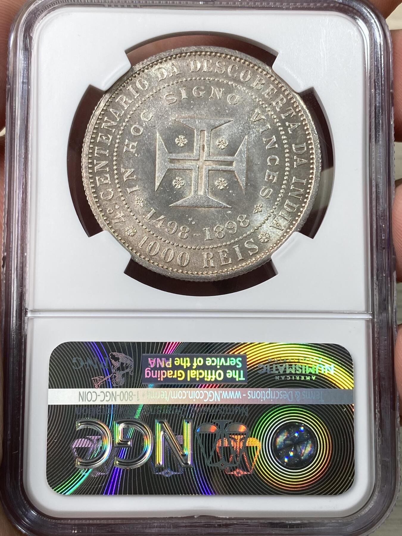 万国钱币拍卖第056期 NGC MS64  1898年葡萄牙1000雷亚尔大银币 纪念发现印度400周年 高分好状态 实物pl感 原银强霜光 打制优异 正面:葡萄牙国王卡洛斯一世和王后阿梅莉侧身半身像 背面:基督勋章十字架，四角有玫瑰花饰，周围有文字。此纪念币是为了纪念瓦斯科·达·伽马于1498年抵达印度。 这位葡萄牙航海家于1497年7月8日从里斯本出发，并于1498年5月2日经好望角经海路抵达印度卡利库特。