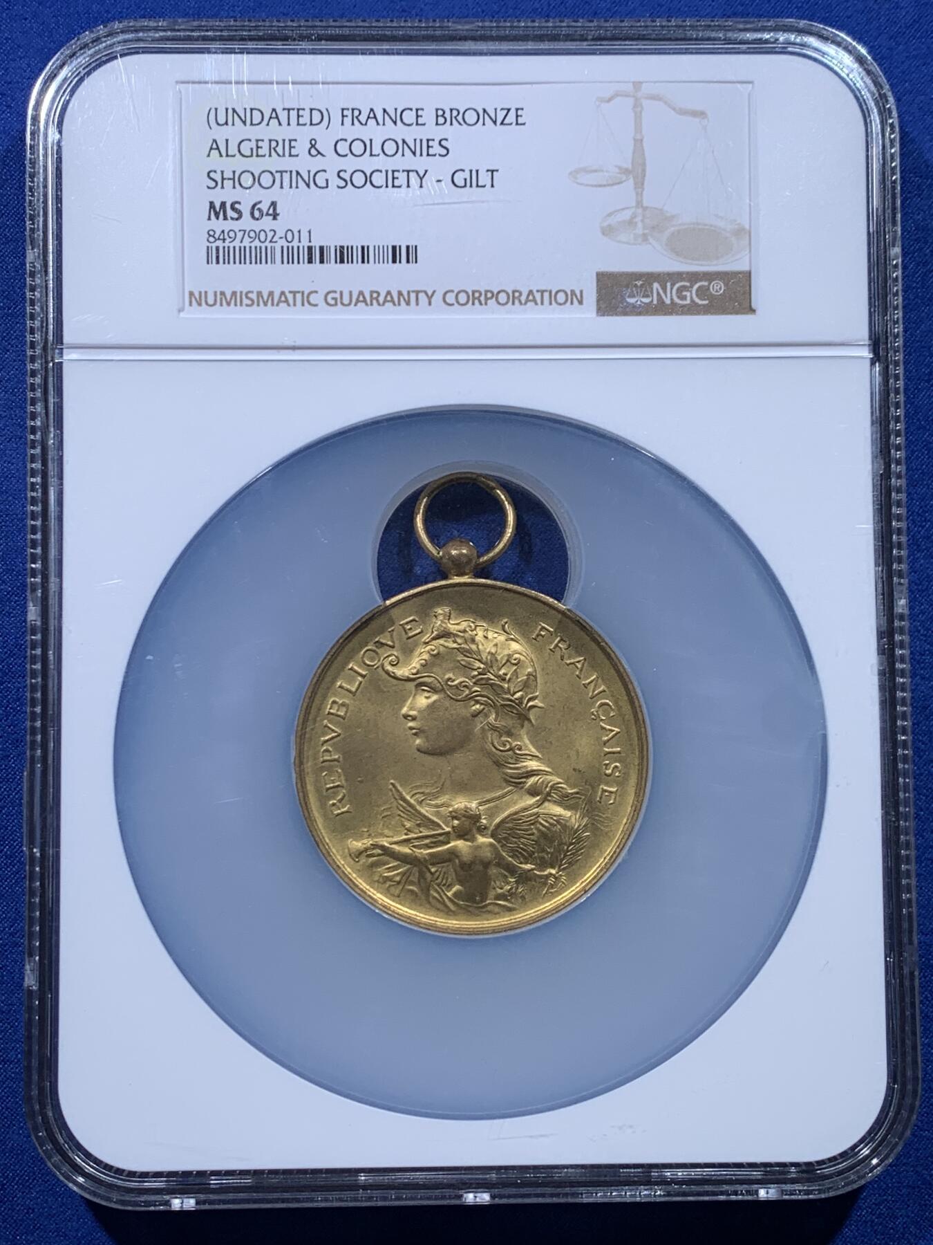 《竞宝斋》第444场 周日，周一，2场连拍 （全场包邮） NGC MS64 约1890年代 法属阿尔及利亚殖民地 射击节镀金大铜章，欧洲射击节常见，殖民地射击节非常稀少。经典的玛丽安娜女神+女性天使，华丽优雅。金水很足，镀层极好。加大加厚盒装，收藏级品质