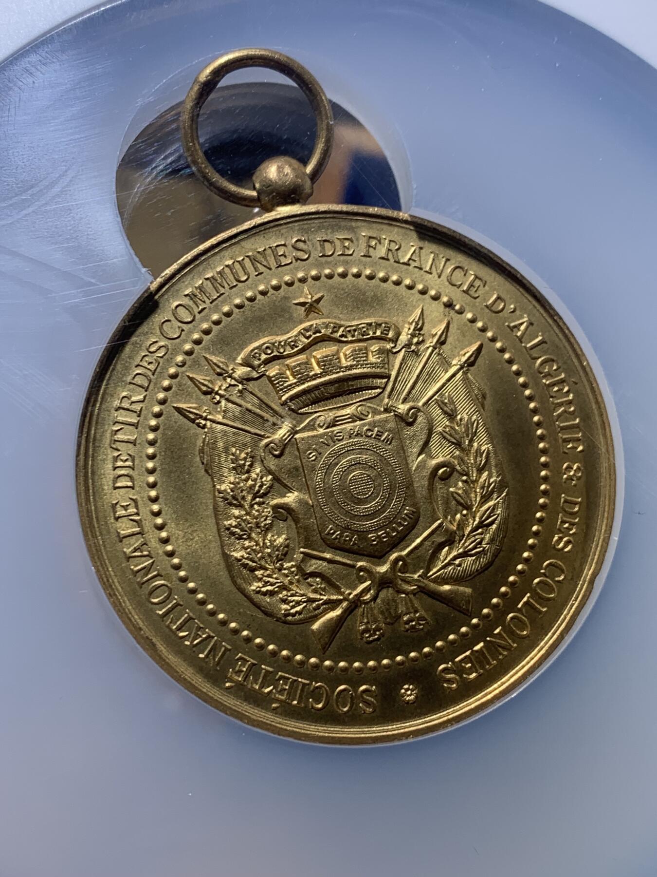 《竞宝斋》第444场 周日，周一，2场连拍 （全场包邮） NGC MS64 约1890年代 法属阿尔及利亚殖民地 射击节镀金大铜章，欧洲射击节常见，殖民地射击节非常稀少。经典的玛丽安娜女神+女性天使，华丽优雅。金水很足，镀层极好。加大加厚盒装，收藏级品质